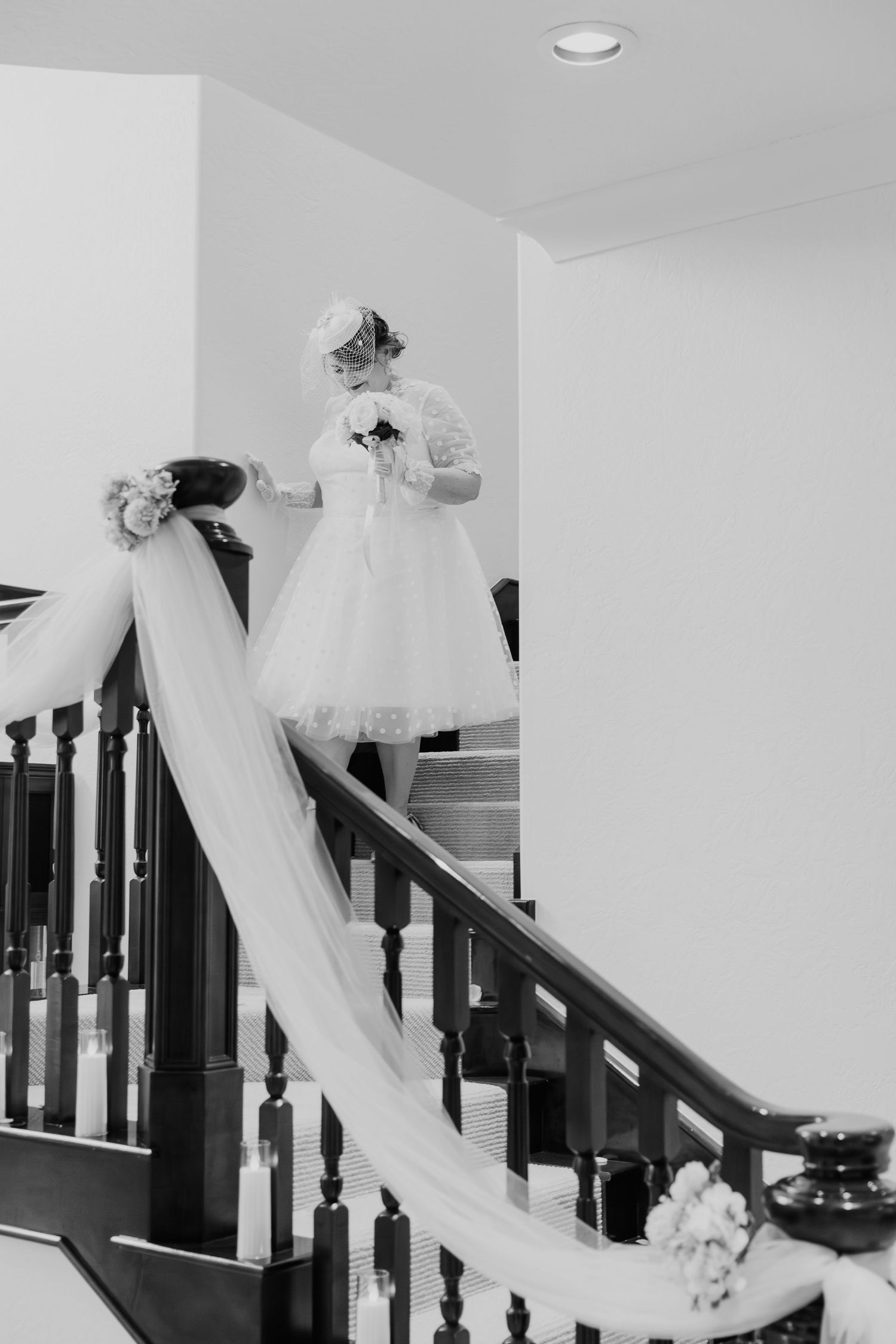 A black and white wedding photo showing a long white veil gracefully draped down a staircase railing.