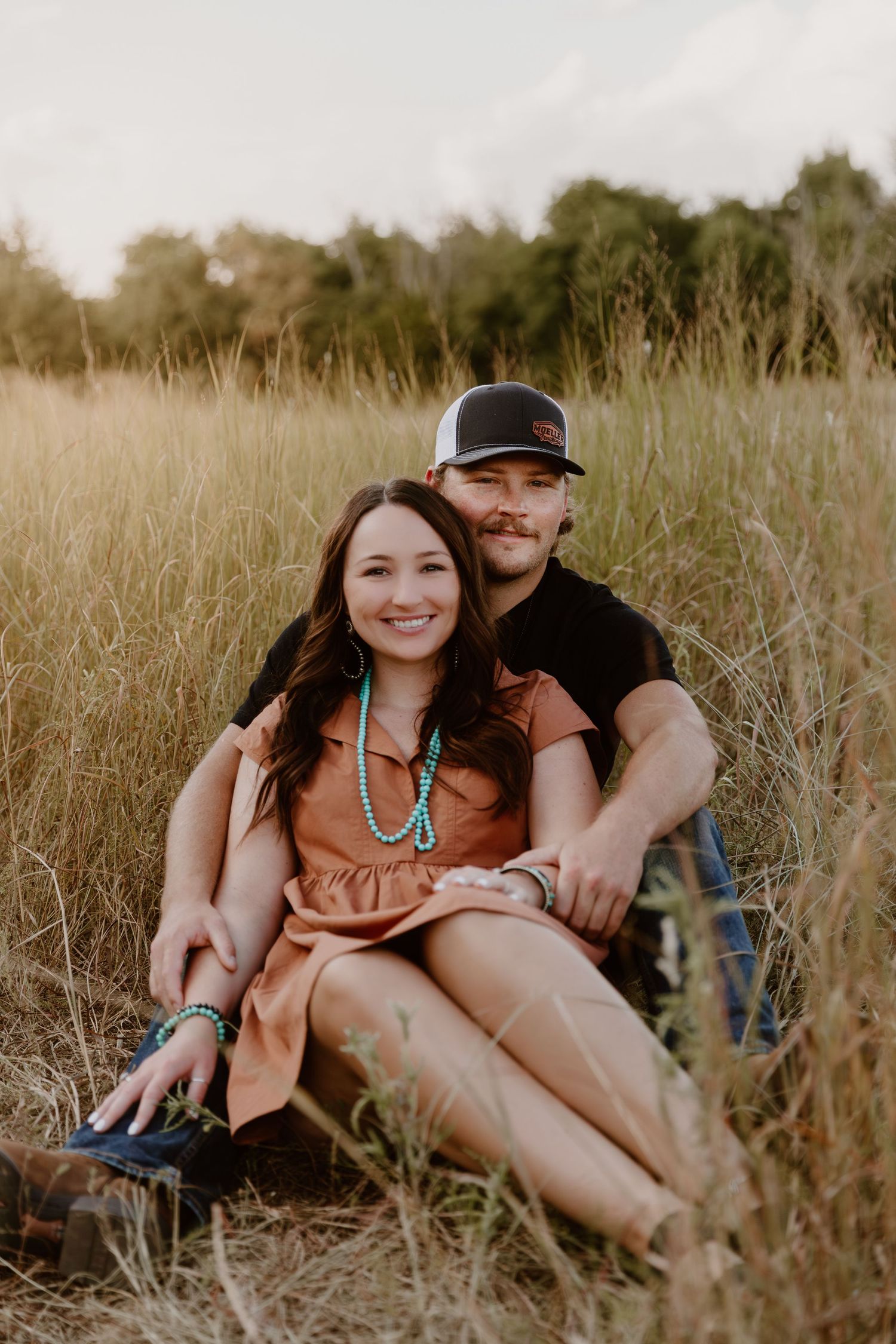 Couple relaxing together in a peaceful meadow with tall grass during golden hour.