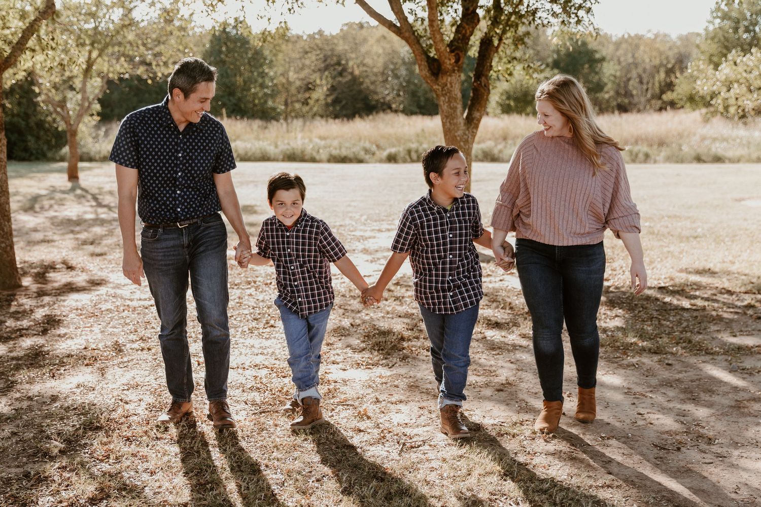 Family walking together on a dirt path through a sunlit outdoor area on an autumn afternoon.