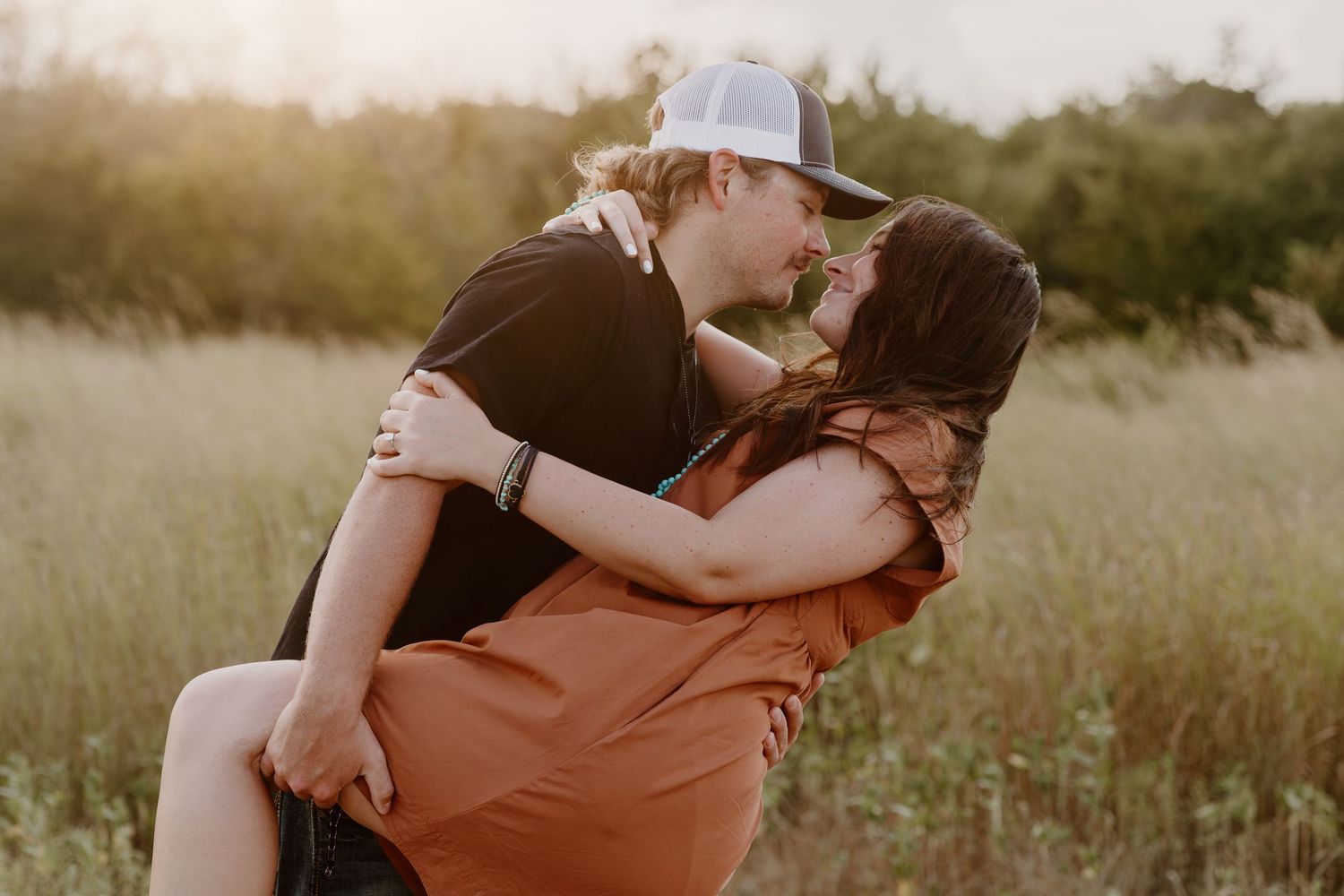 A romantic couple embraces in a sunlit field during golden hour.