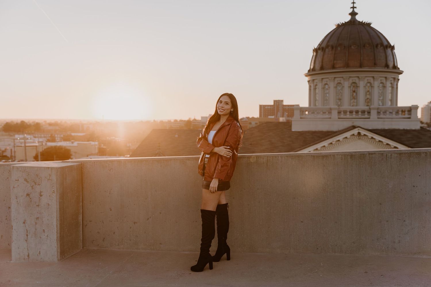 A person poses on a rooftop at sunset with a domed building in the background.