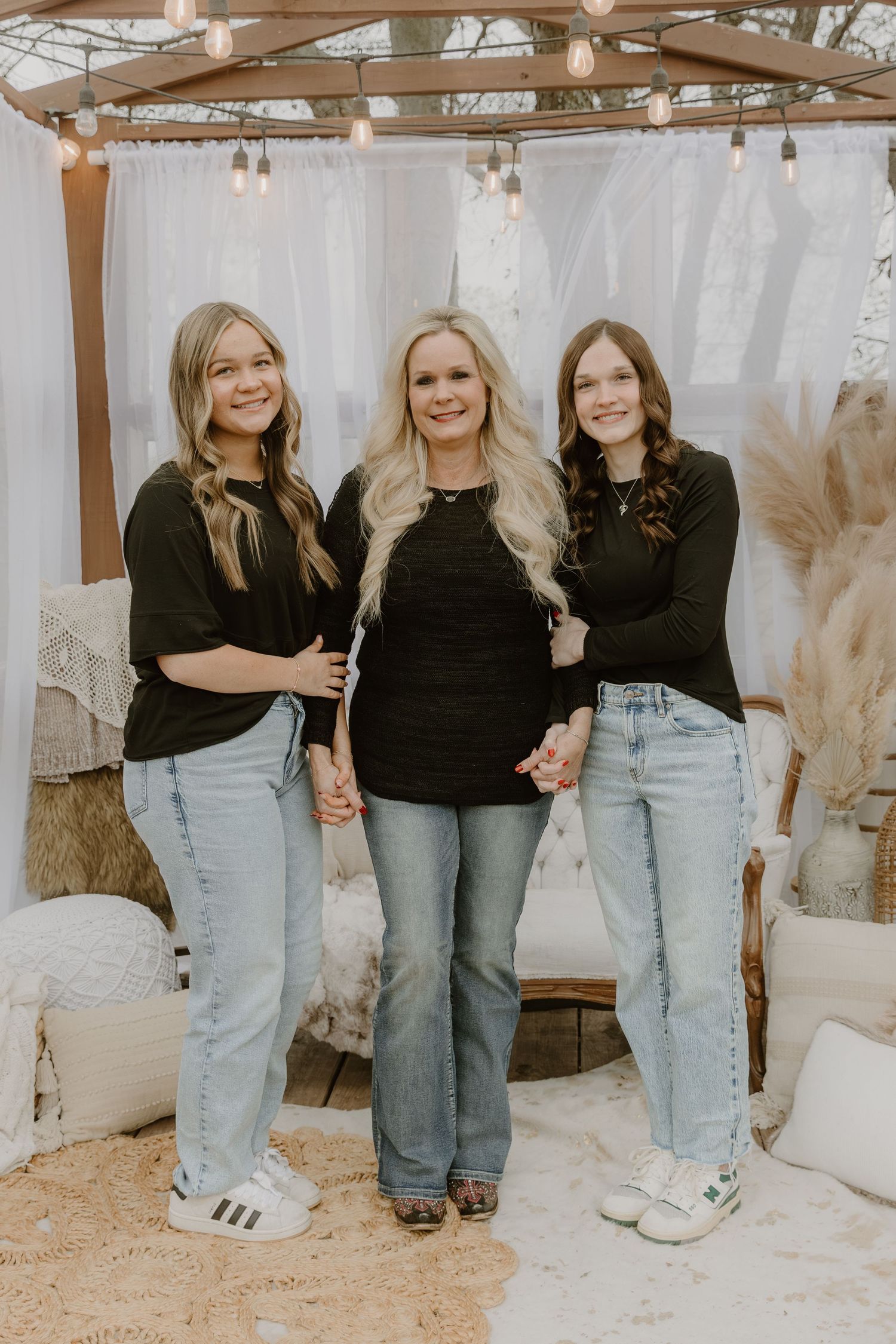 Three friends in matching black tops and light jeans pose together in a rustic outdoor setting.