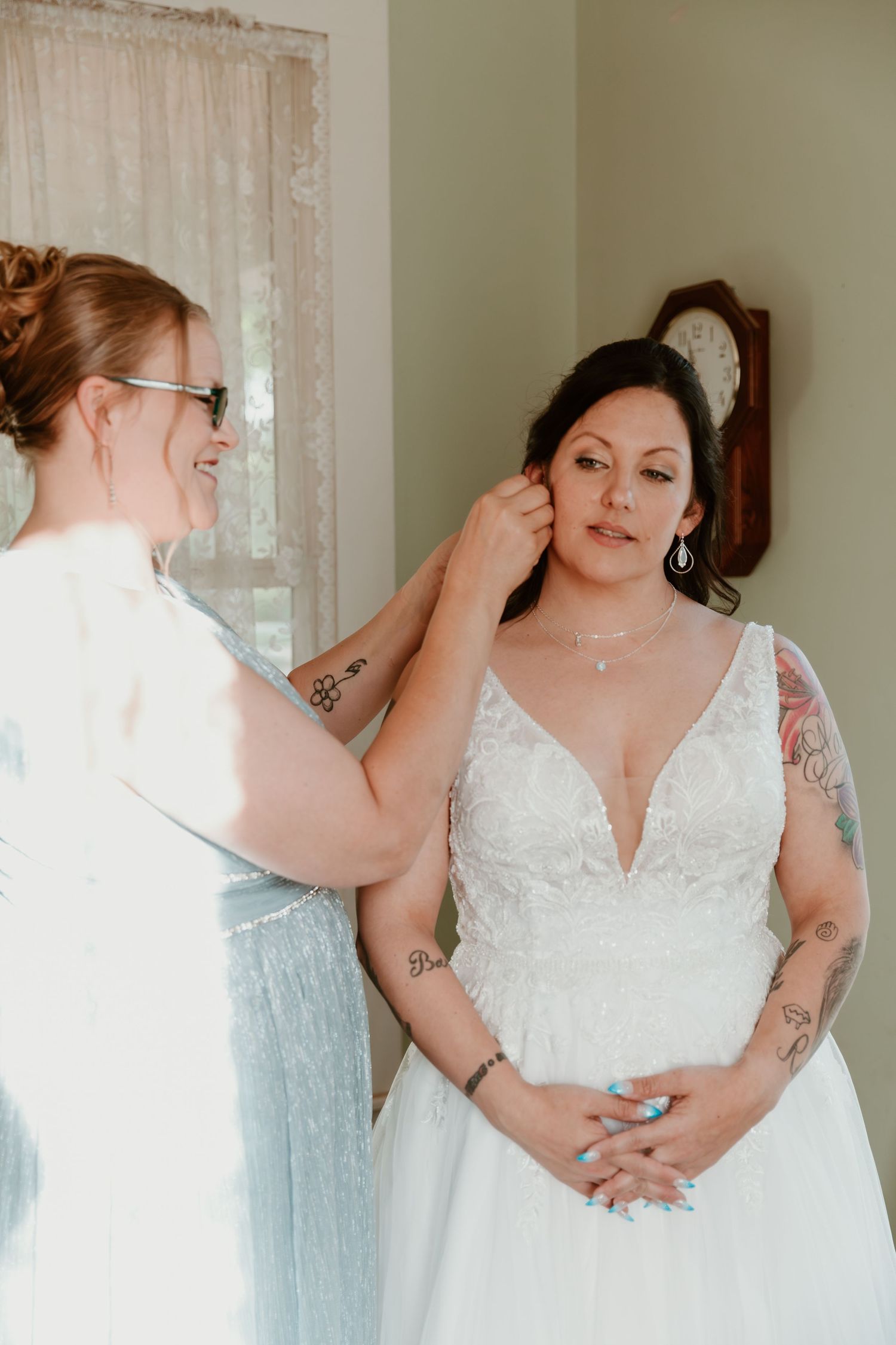 A touching moment of wedding preparation as a bride in a white lace dress gets help with final adjustments.