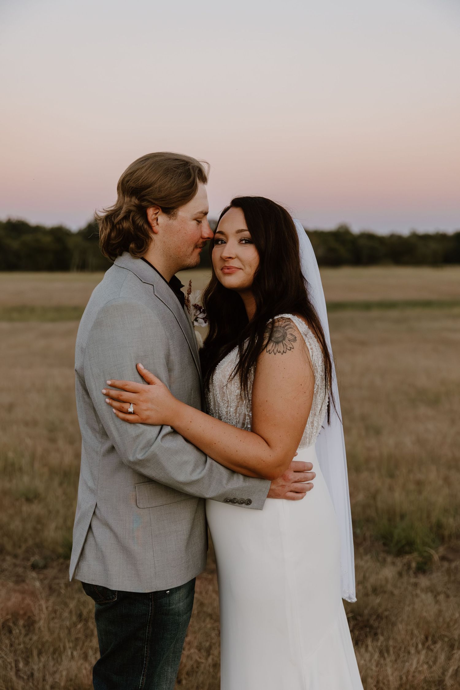 A couple shares an intimate moment in a golden field at sunset wearing wedding attire.