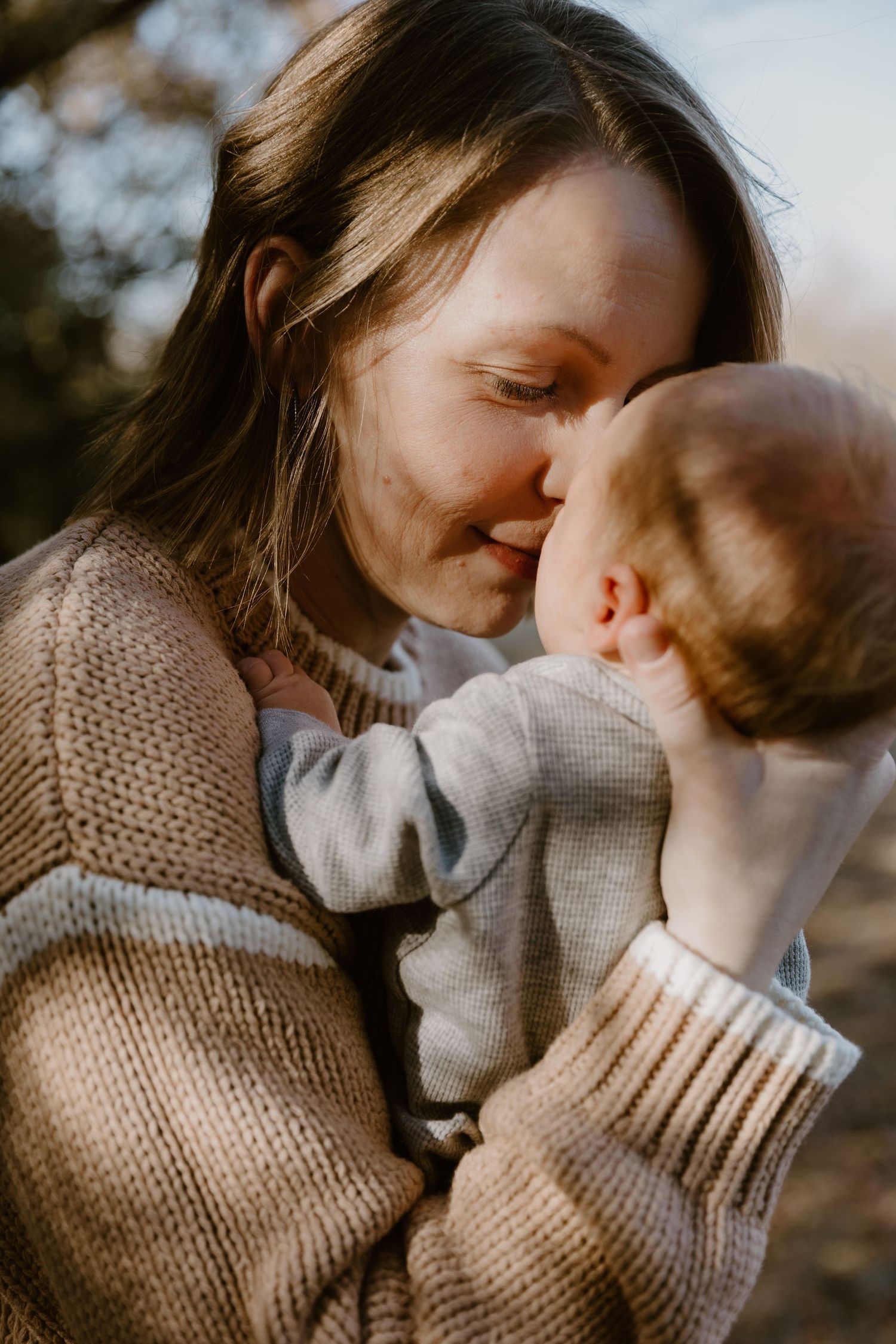 A tender moment between parent and baby wearing cozy knit sweaters in warm autumn light.