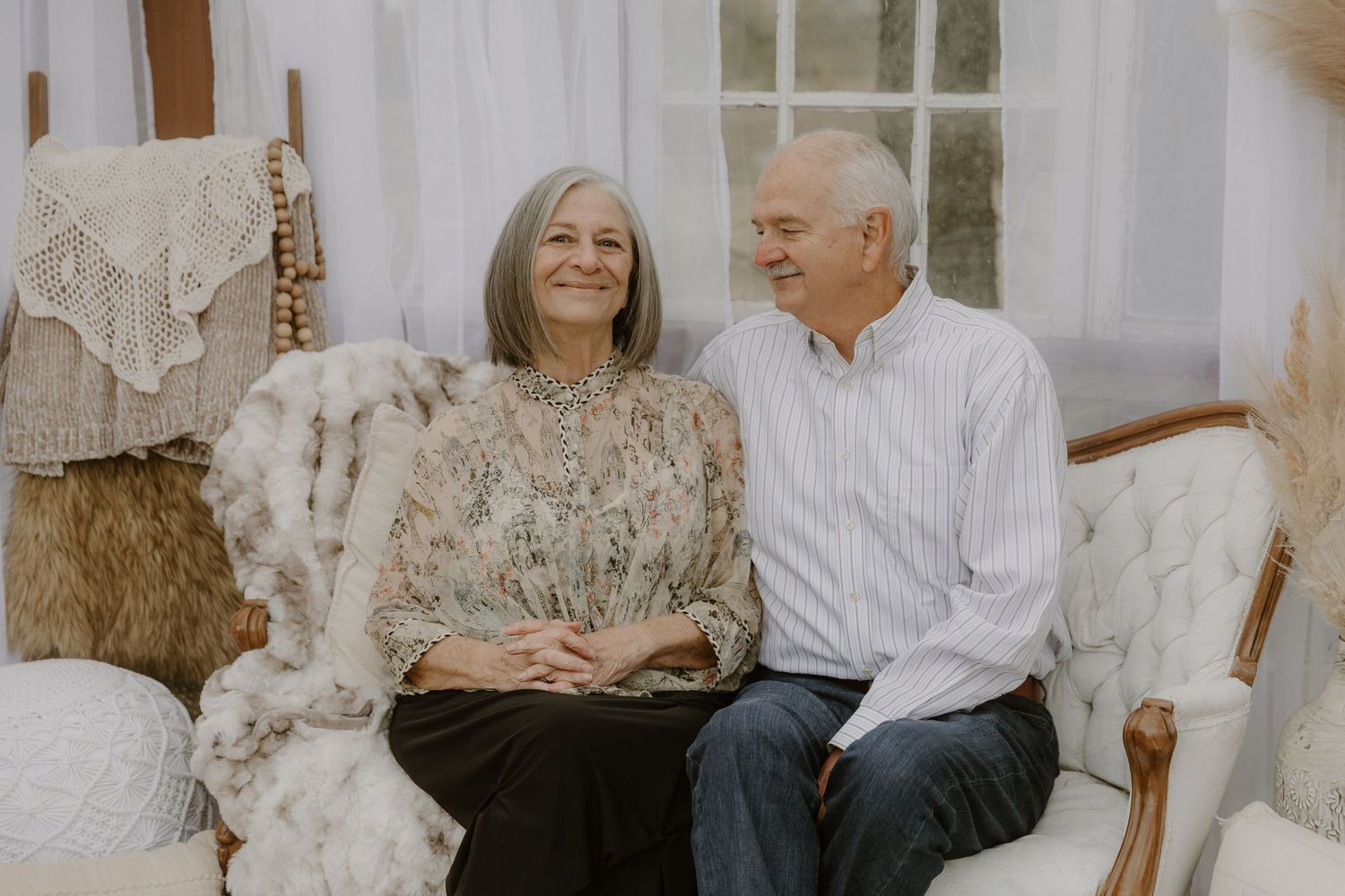 Elderly couple sitting together on a couch in a bright room with white decor.