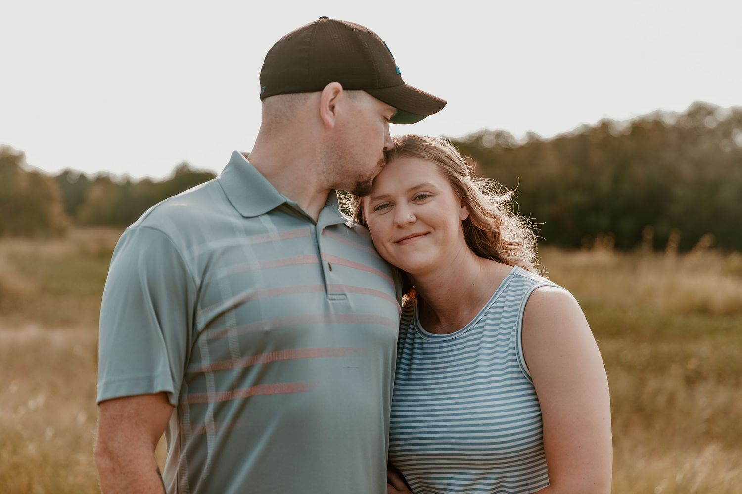 A couple shares an intimate moment together in a grassy autumn field at sunset.