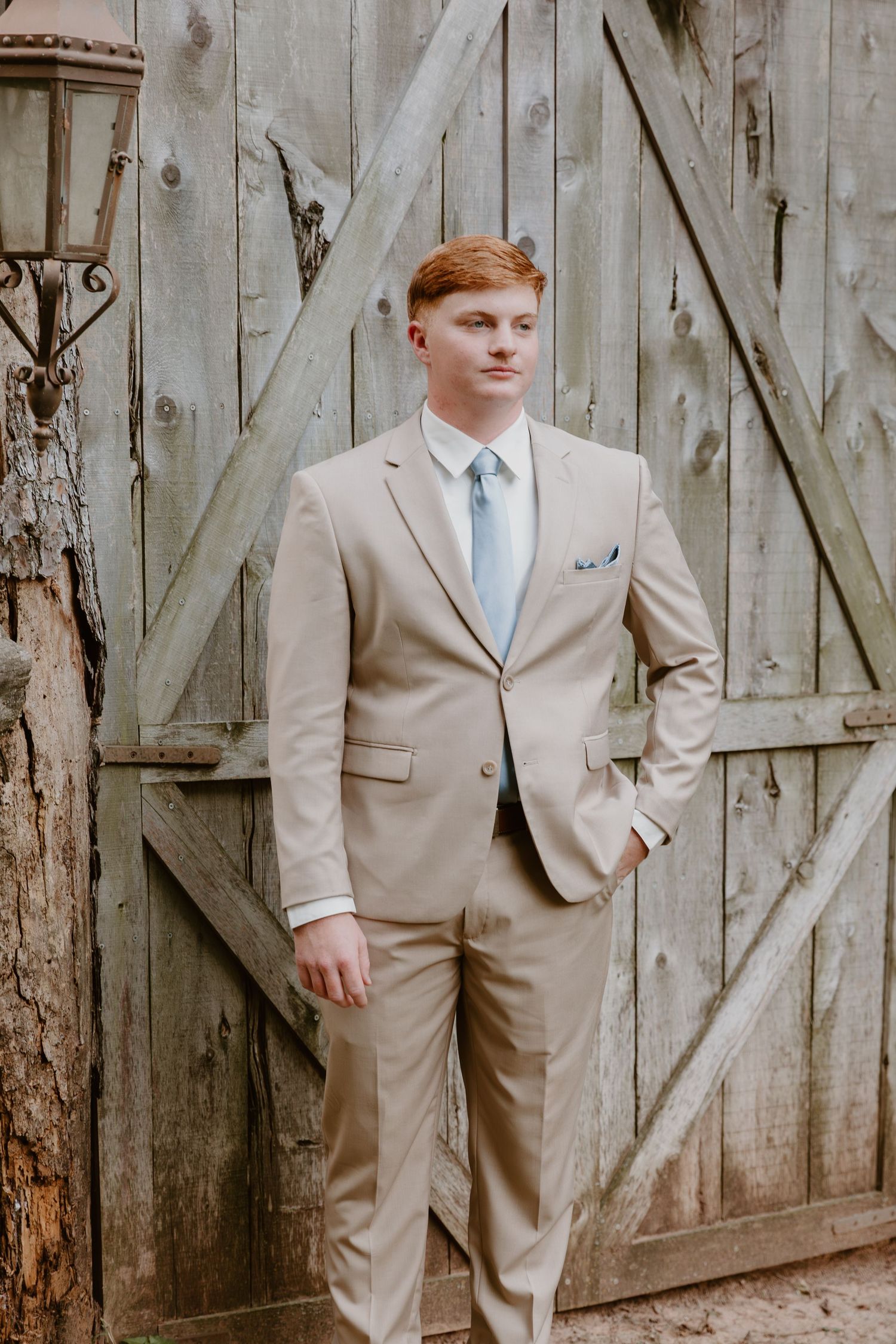 A trio of beige-suited men stand in front of rustic wooden barn doors in formal wedding attire.