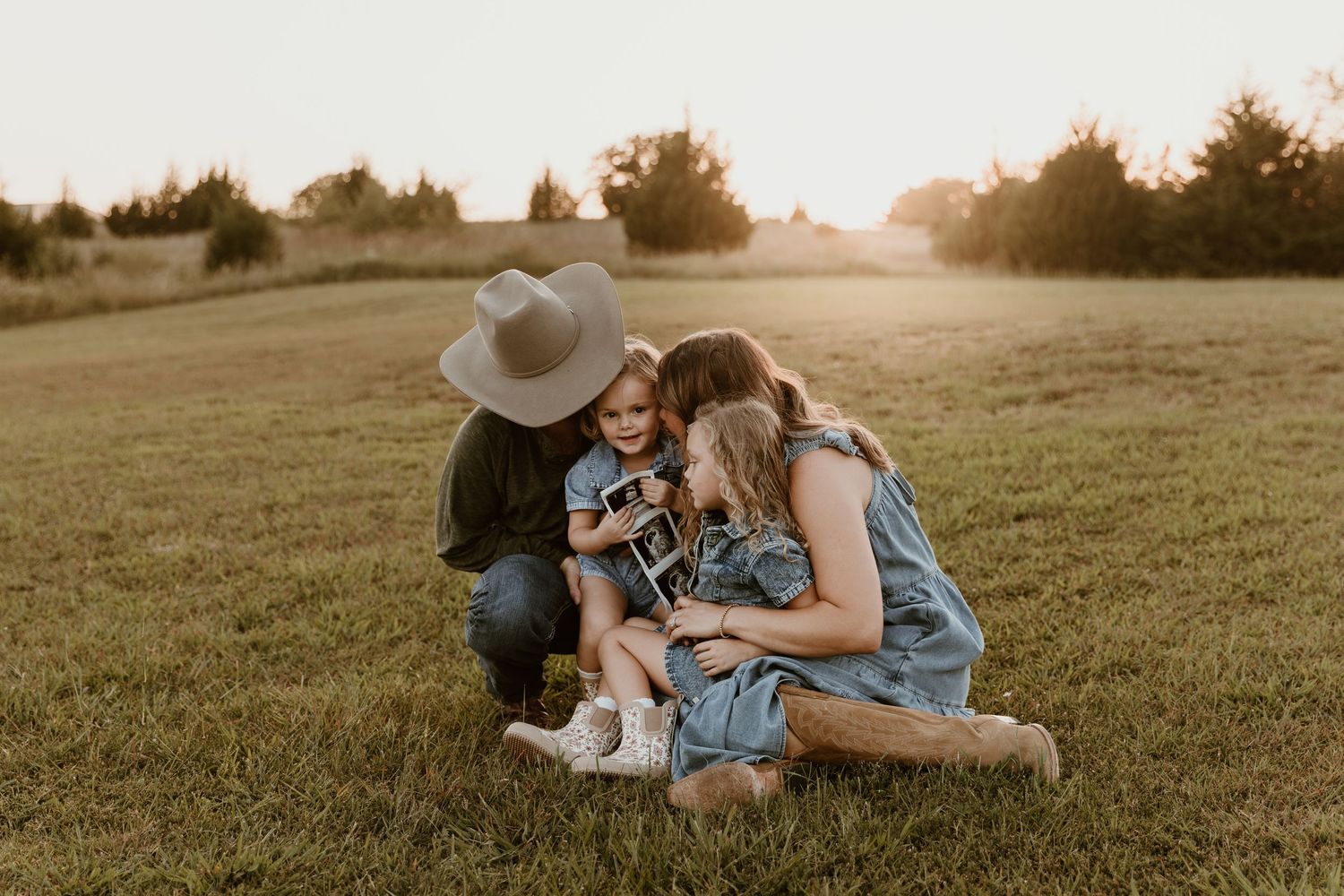 A couple lying in a grassy field at sunset in a romantic embrace.