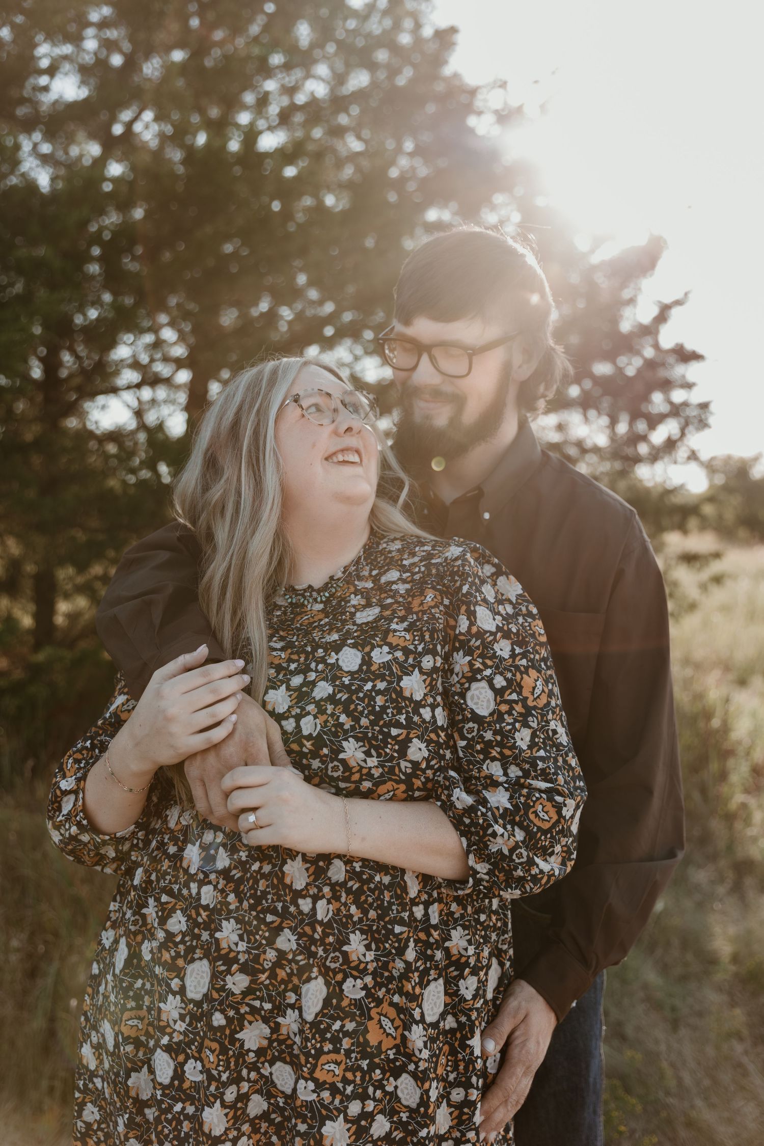 A couple shares joyful laughter together during a golden hour photoshoot in a natural outdoor setting.