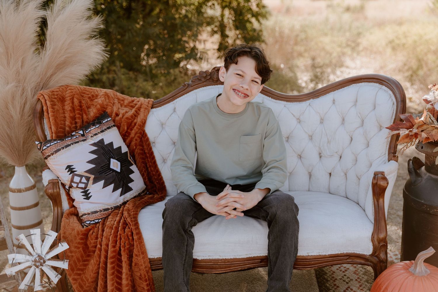 Vintage tufted sofa with burnt orange throw blanket and decorative pillows in an outdoor autumn setting.