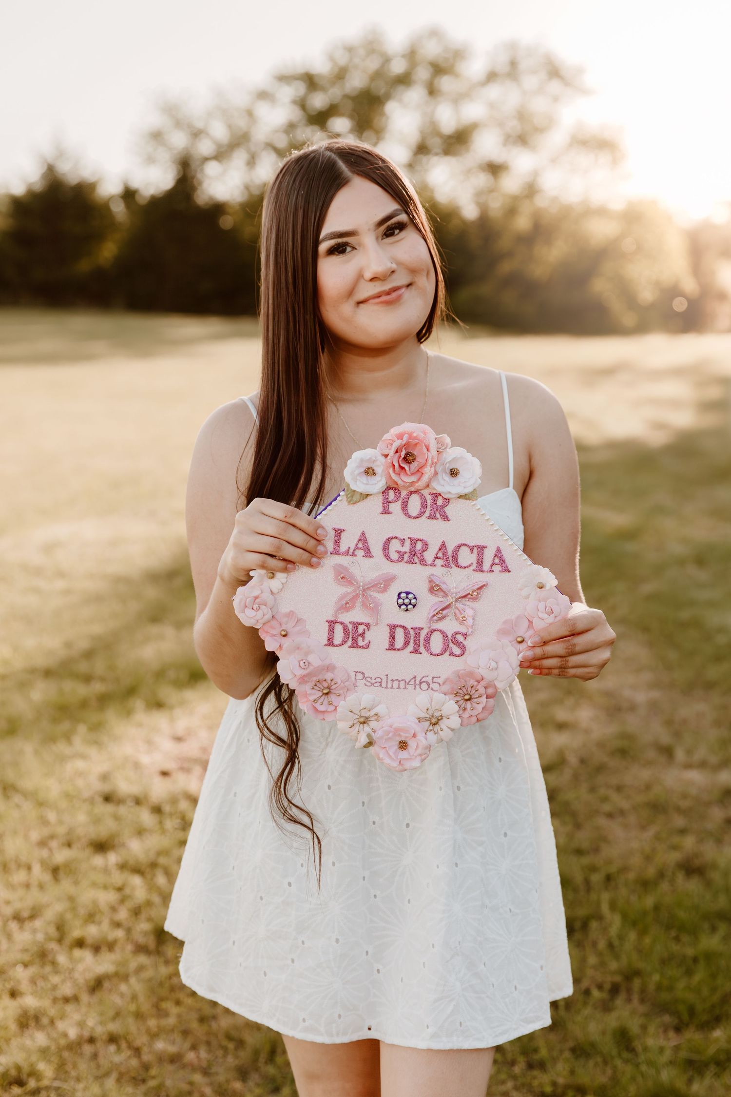 Someone in a white dress holds a pink floral sign with Spanish text 