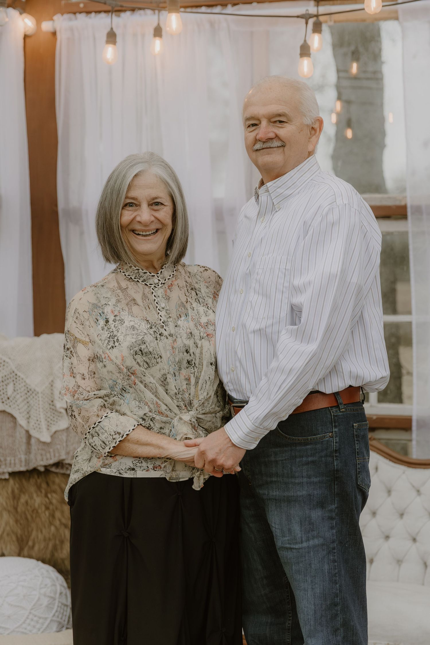 A couple in coordinated outfits embracing and smiling in a romantic indoor photoshoot with warm lighting.