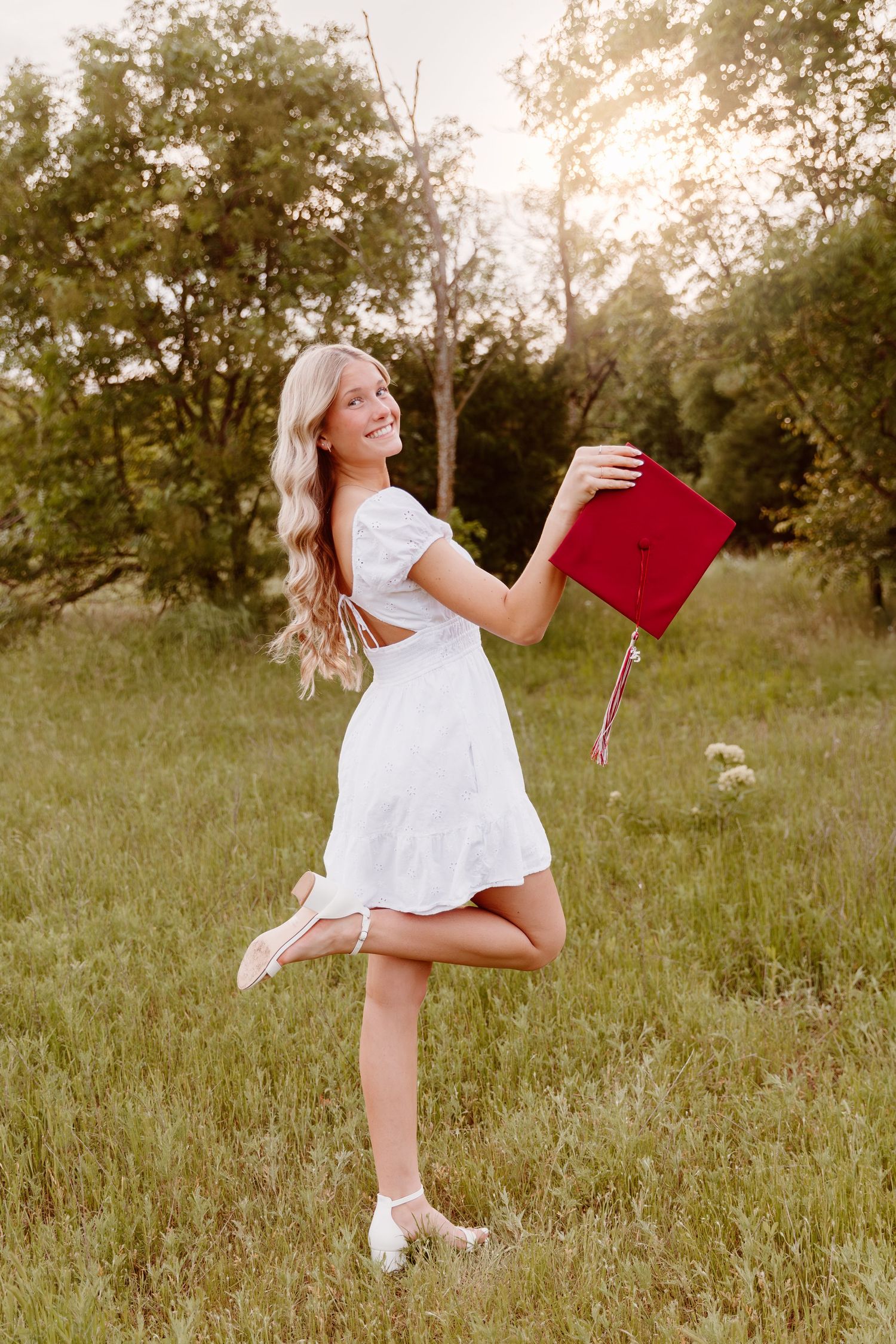 A person in a white dress dances and twirls through a sunny meadow holding a red book at golden hour.