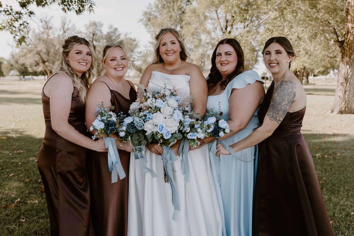 Wedding party in light blue bridesmaid dresses holding bouquets with eucalyptus and white flowers in outdoor setting.