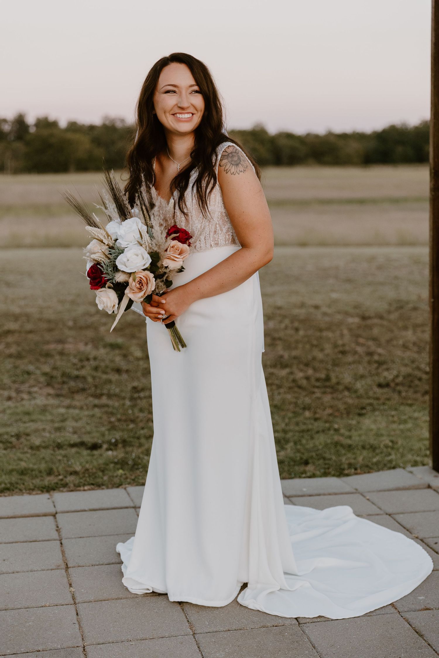 A bride in a flowing white dress sits gracefully on stone pavers while holding a bouquet during an outdoor photo session.