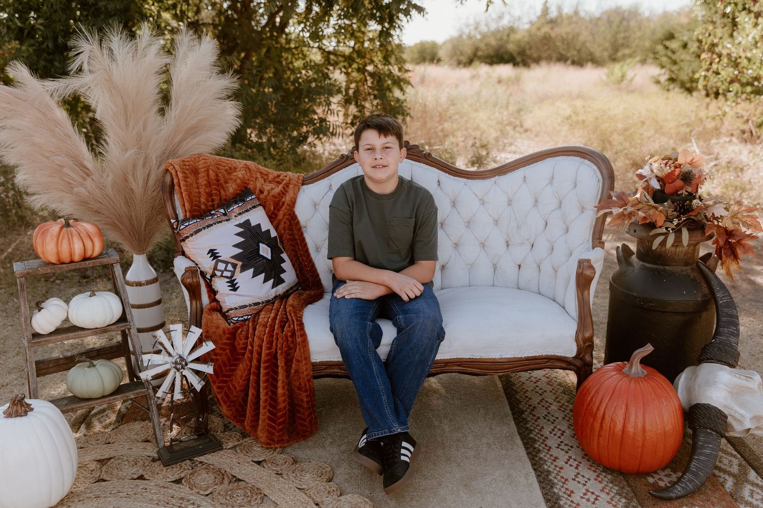 Romantic fall photoshoot setup with vintage furniture, pumpkins and warm autumn colors in natural setting.