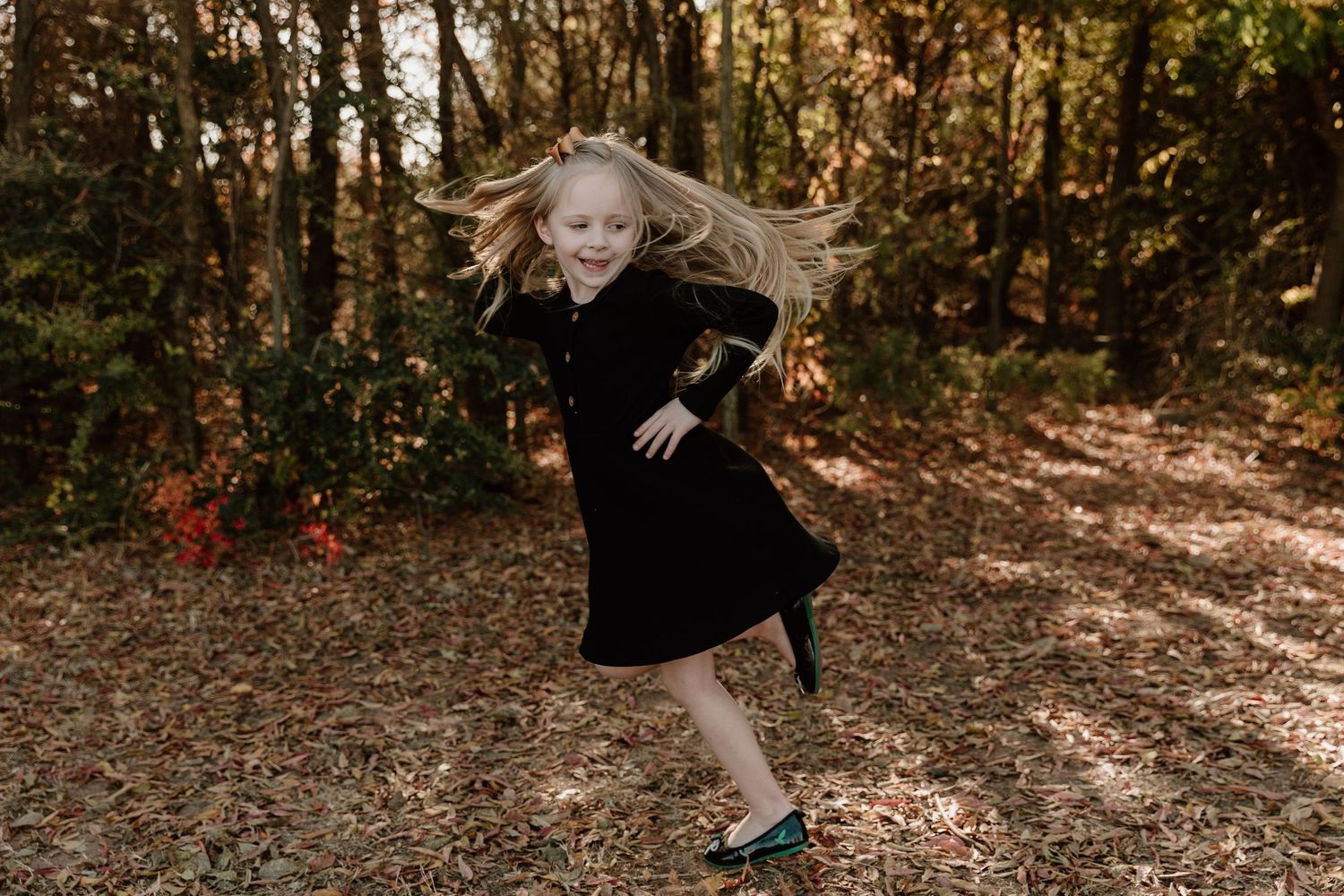 A person in a black dress twirls gracefully in a sunlit autumn forest setting.