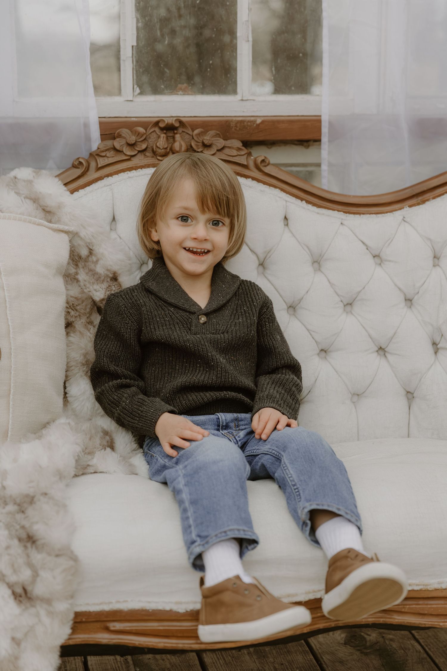 Child sitting comfortably on an elegant white tufted sofa wearing a dark sweater and jeans.