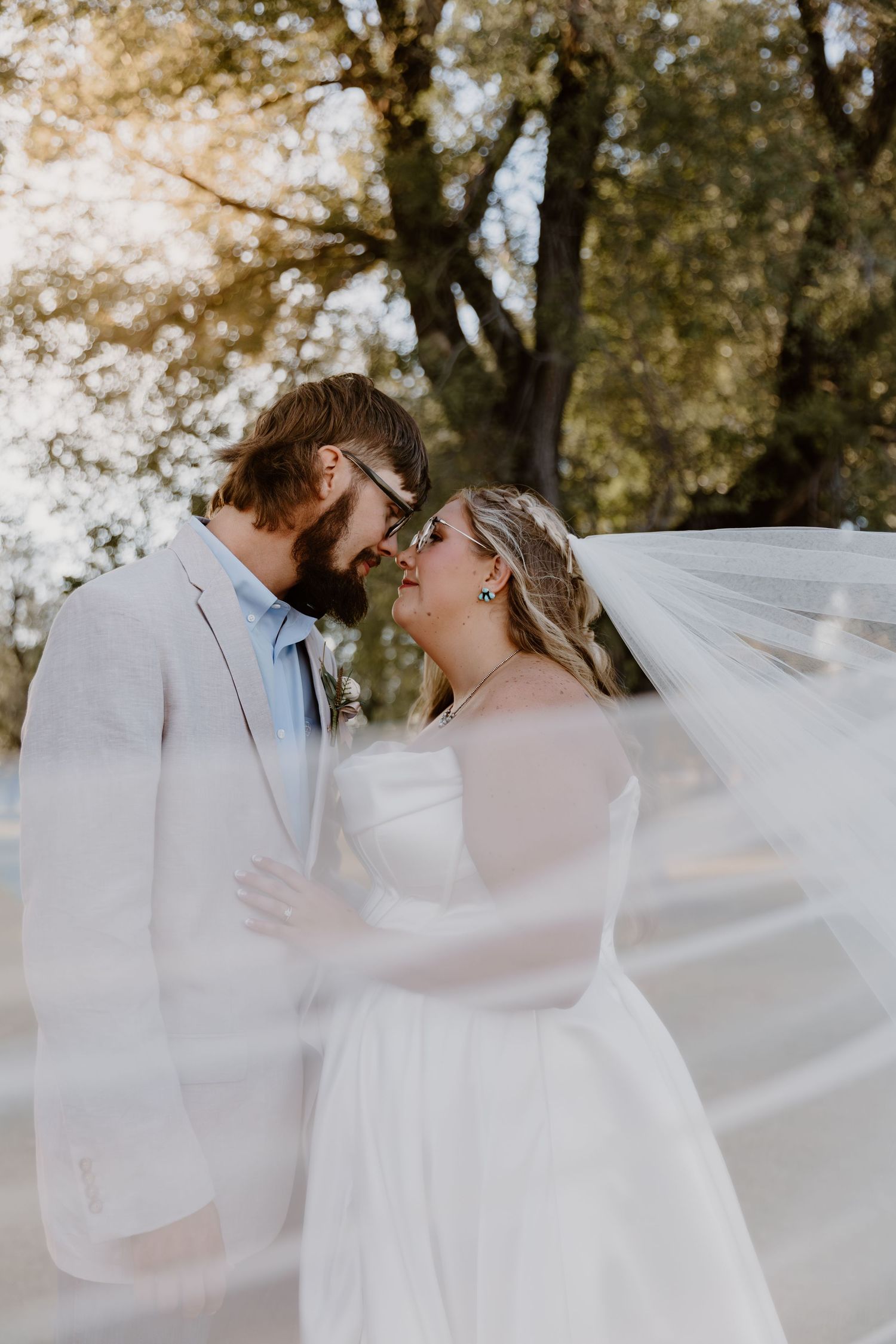 A couple shares an intimate moment under a flowing white veil in an outdoor garden setting.