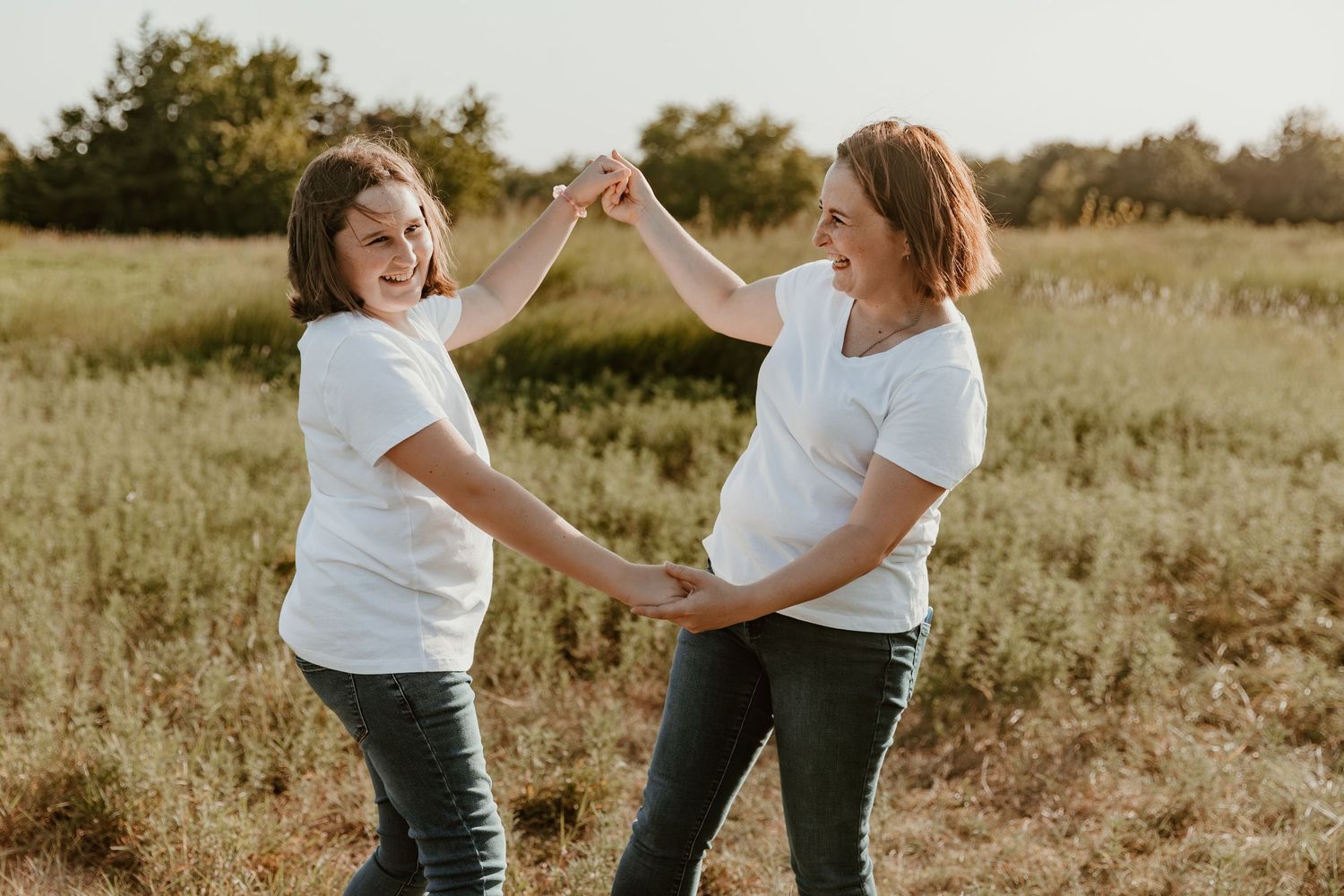A field at sunset provides a golden backdrop for two figures sharing playful moments and joyful dancing.