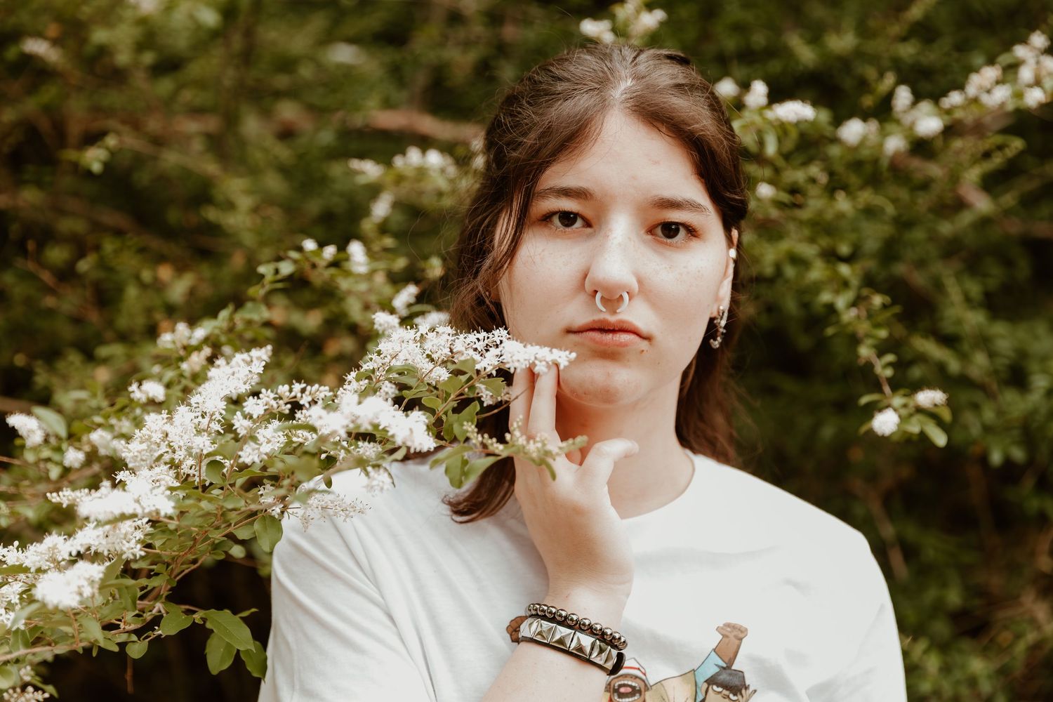 Portrait in a white t-shirt amidst blooming white spring flowers against a natural garden backdrop.