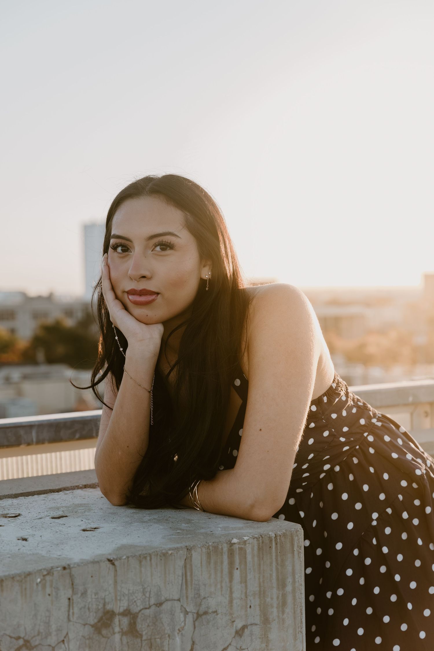A person in a polka dot dress poses on a concrete ledge during golden hour sunset.