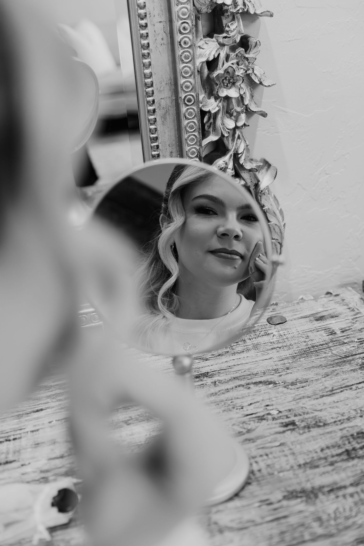Artistic black and white reflection in an ornate vintage mirror showing curled blonde hair and elegant styling details.