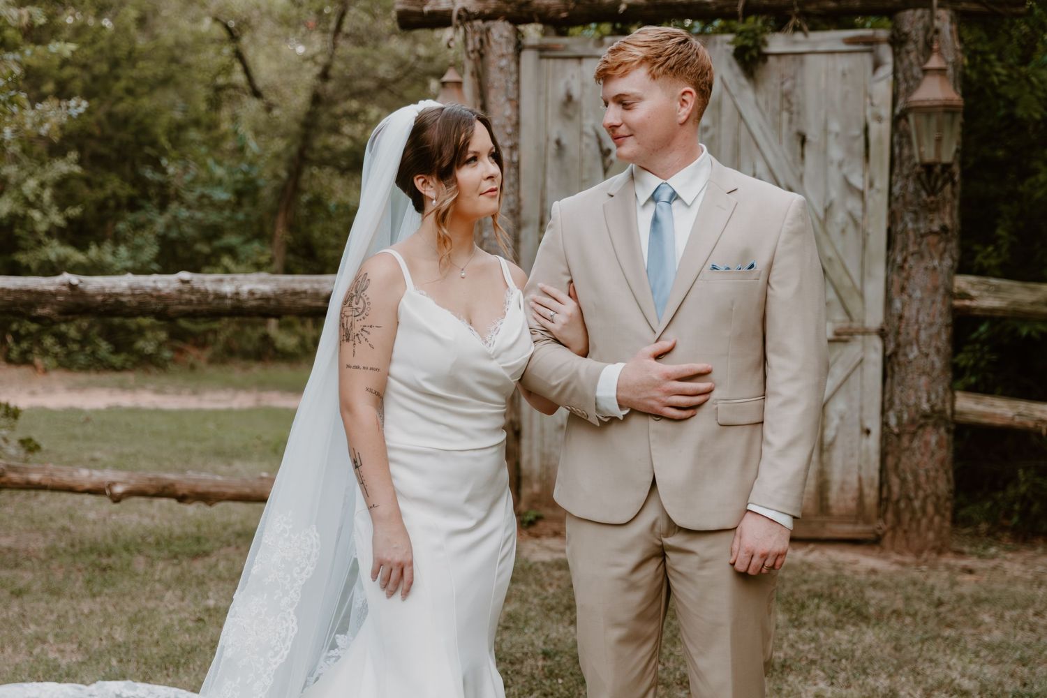 A newlywed couple poses romantically in a rustic outdoor setting with natural woodland backdrop.