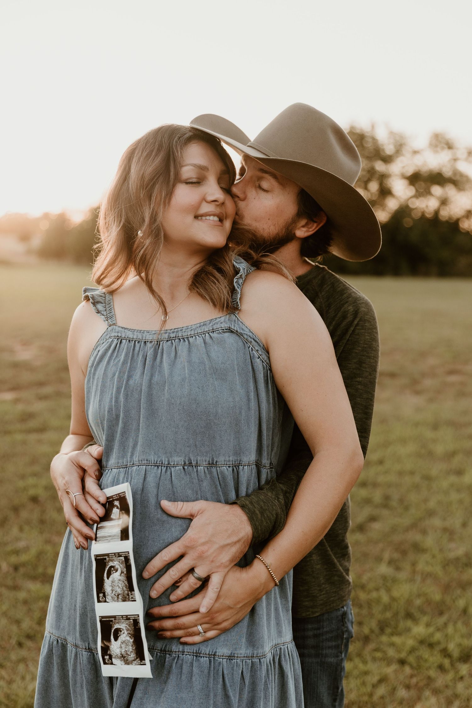A series of intimate maternity photos showing a couple embracing in a sunlit field while holding an ultrasound photo.