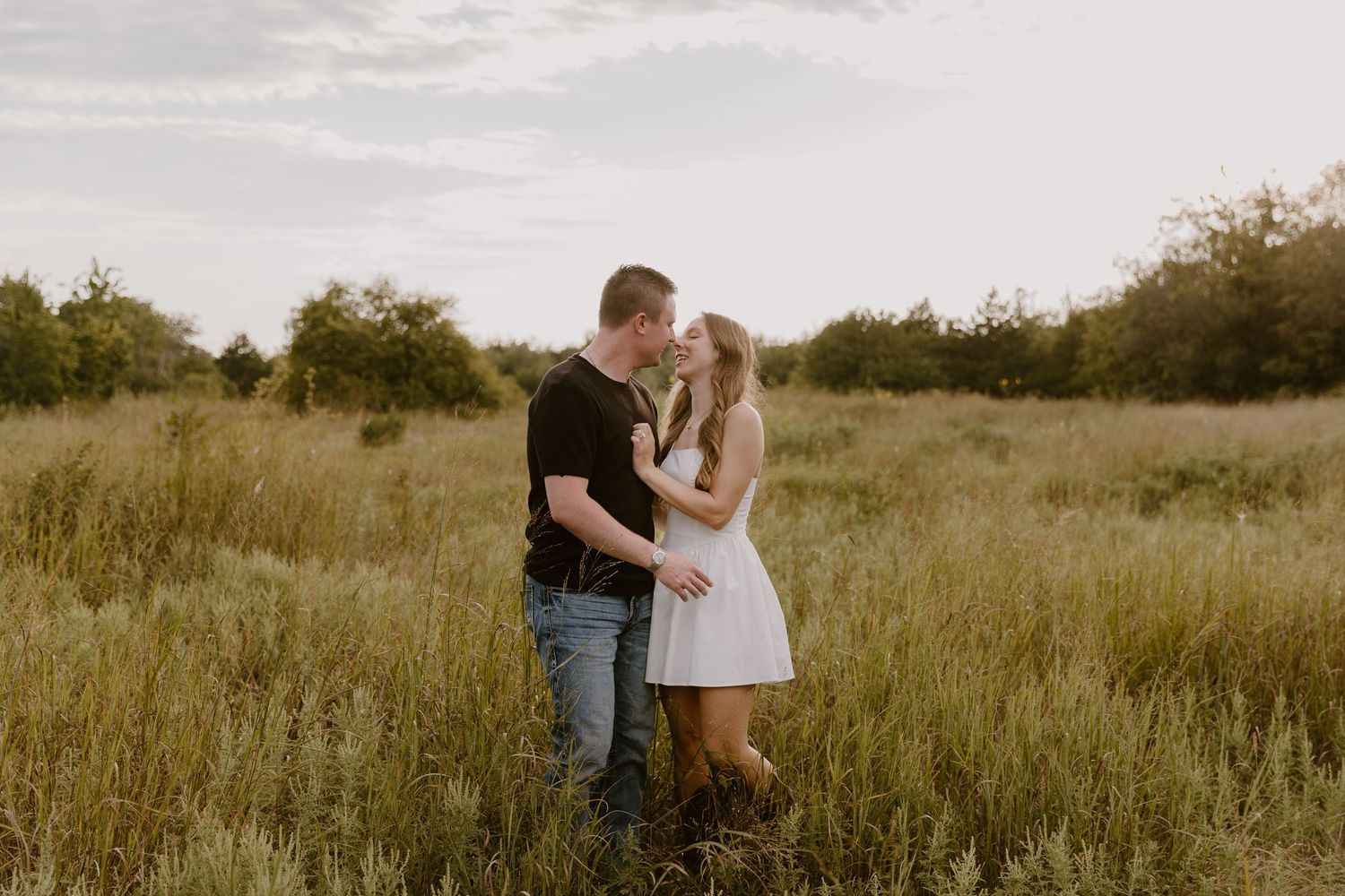 Couple embraces lovingly in a serene golden field during sunset creating a romantic rustic atmosphere.