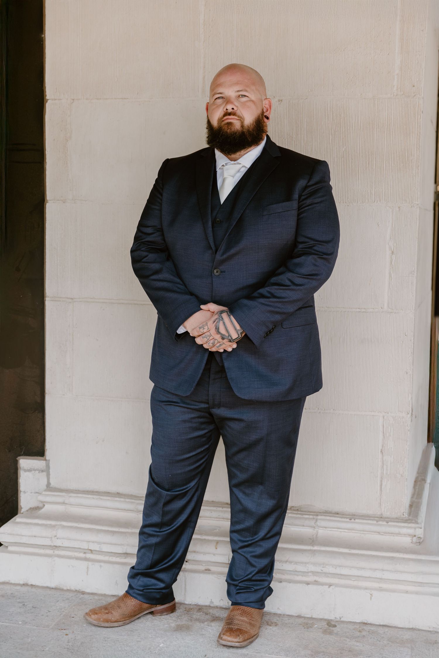 A person in a navy blue suit and brown dress shoes stands against a white wall in five different cropped poses.