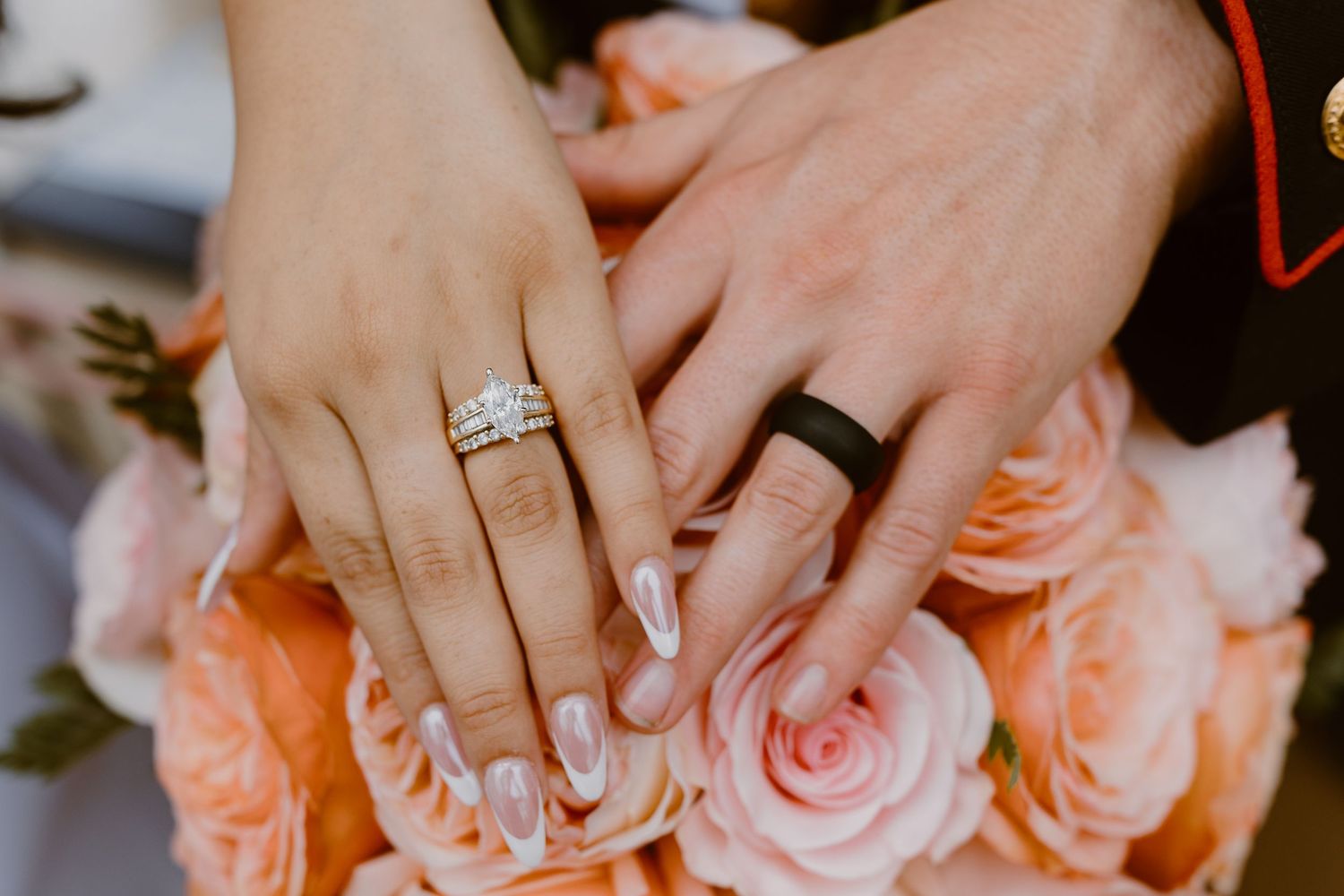Close-up view of hands holding coral and peach roses with diamond engagement ring prominently displayed.