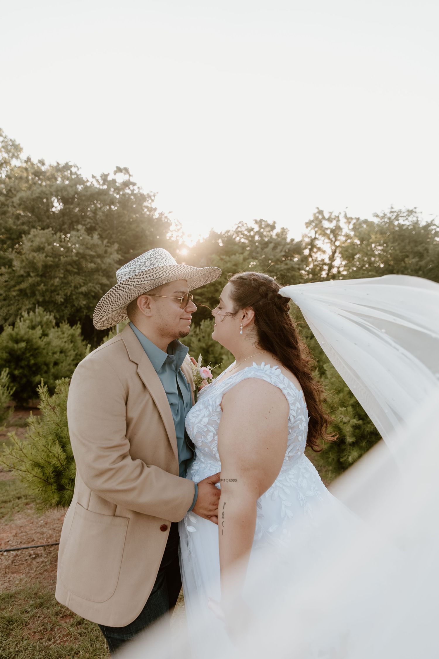 Bride and groom gazing at each other in golden hour light, veil flowing in the breeze.