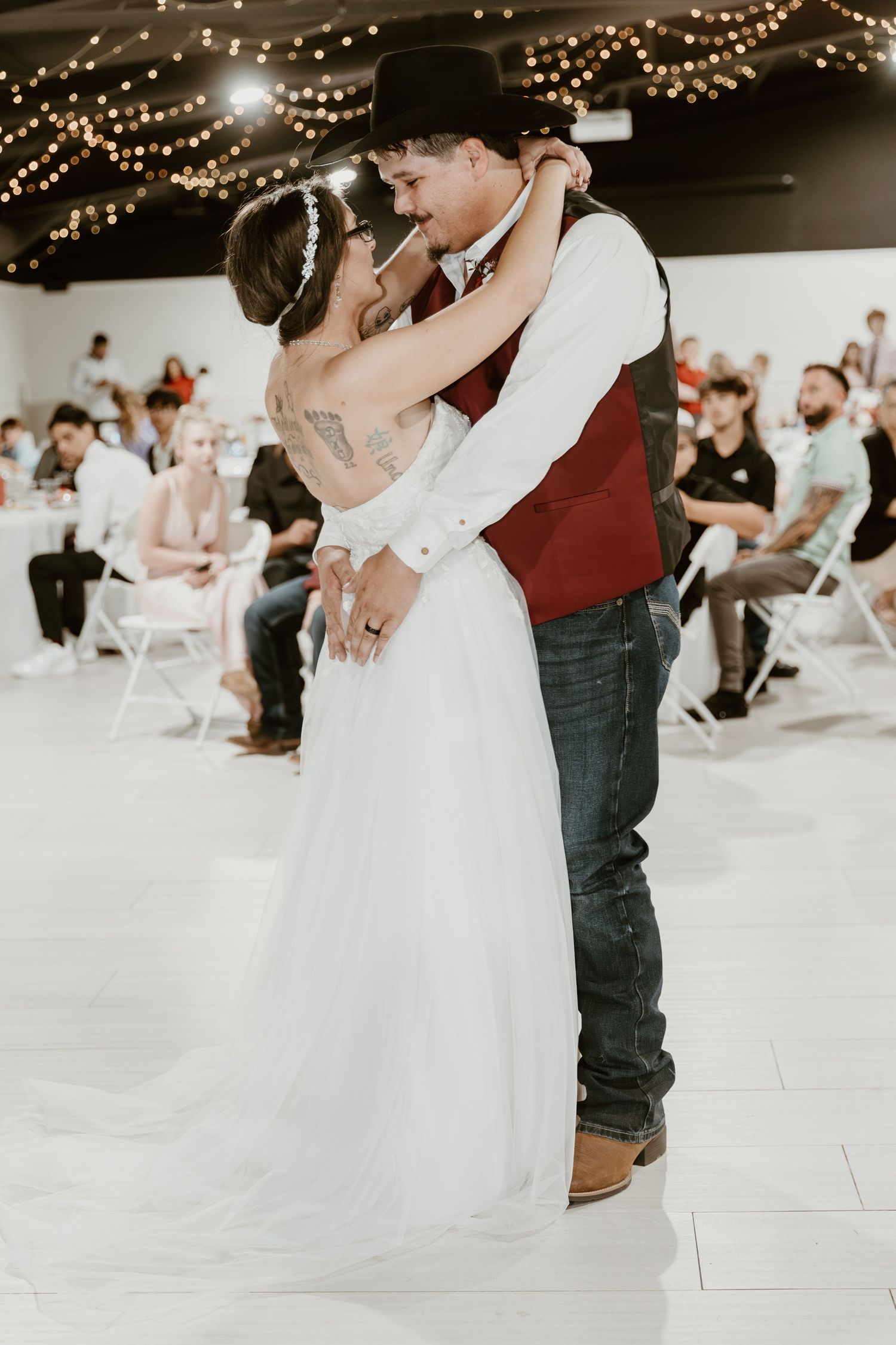 A couple shares a romantic first dance at their rustic wedding reception under twinkling string lights.