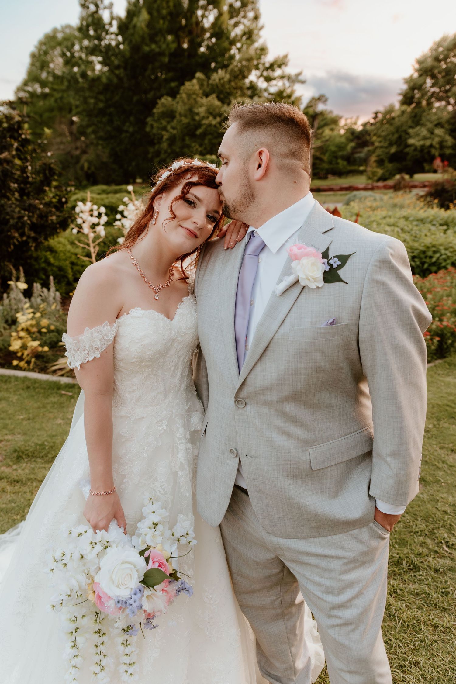 Elegant wedding couple embracing in garden setting with bride holding delicate floral bouquet.