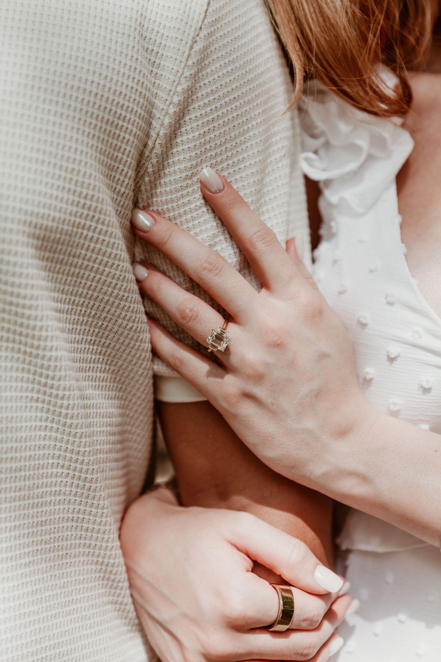 Close-up of hands with wedding rings touching against a white textured fabric background.