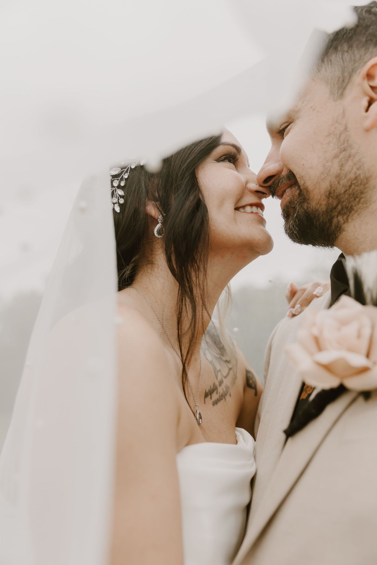 A smiling bride and groom lean in for a kiss under a flowing white veil on their wedding day.