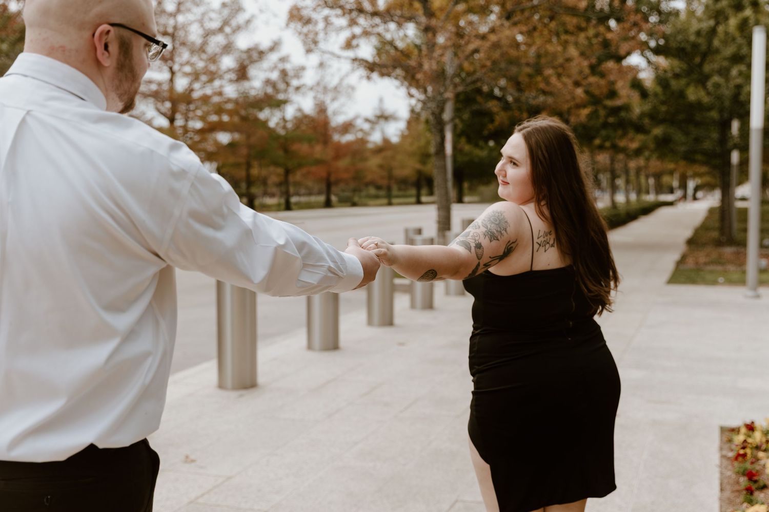 A couple in white and black outfits share a romantic moment during an autumn engagement photoshoot in a park.