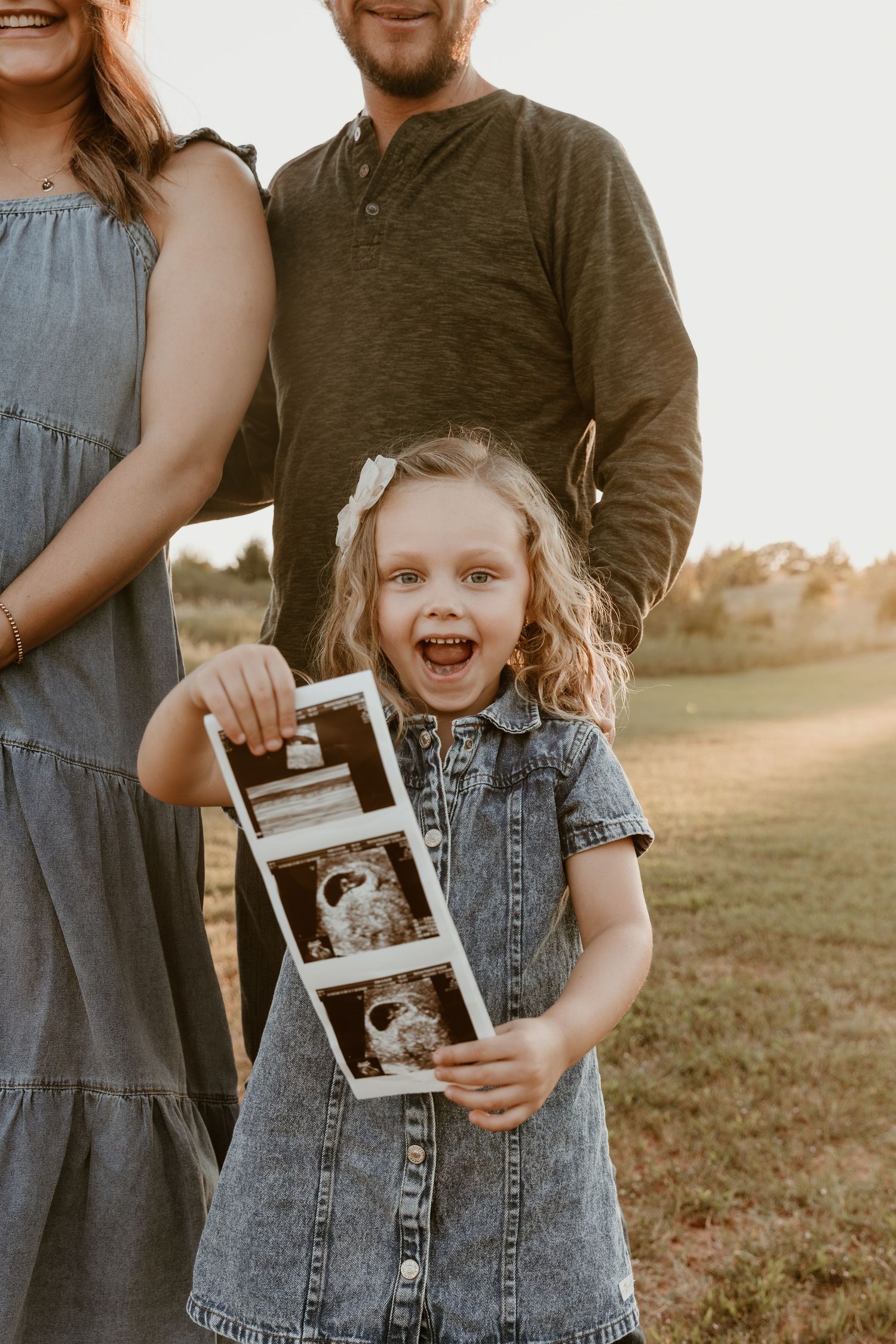 A family shares a joyful moment while holding ultrasound photos in an outdoor setting.