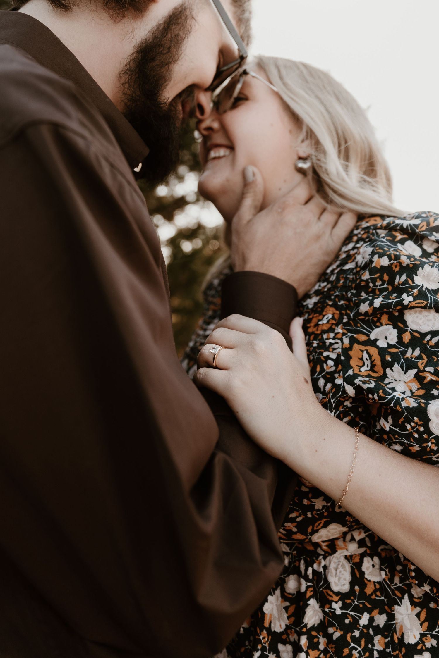 A romantic couple shares a tender kiss while wearing a floral dress and dark clothing in an intimate photoshoot.
