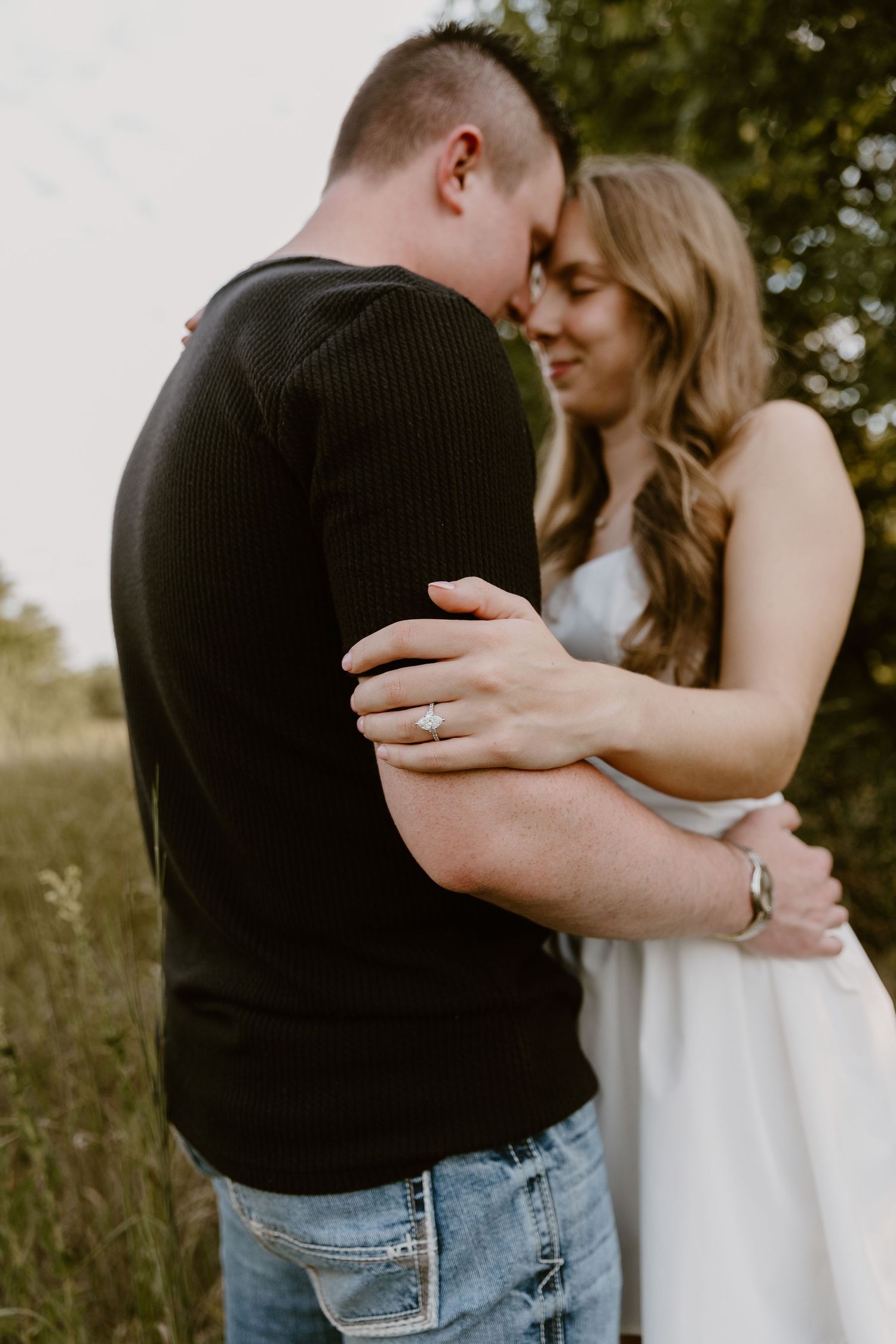 A romantic couple embraces in a meadow at sunset, with the woman in white and man in black.