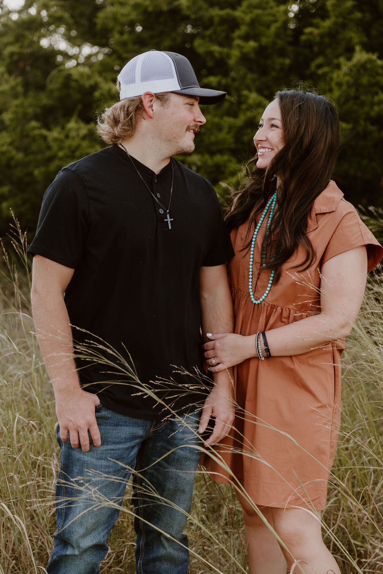 A couple in casual attire shares intimate moments together in a field of tall grass at sunset.