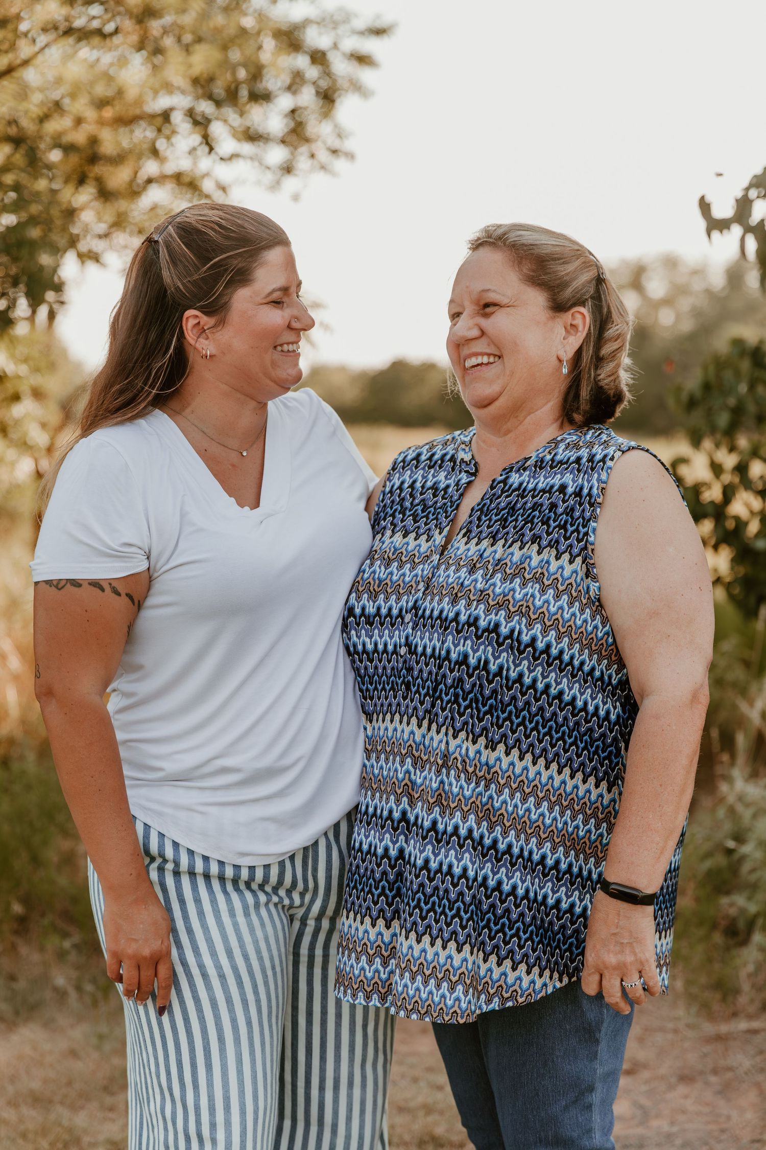 Two figures share a joyful moment outdoors in natural lighting with trees visible in the background.