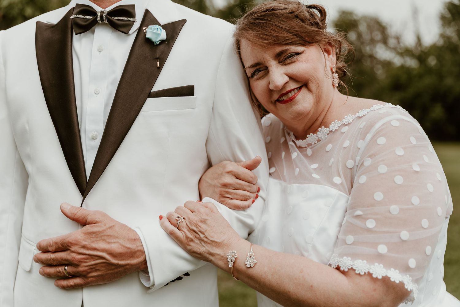 A person in a polka dot dress holds hands with someone wearing a white tuxedo jacket with brown lapels at a wedding.