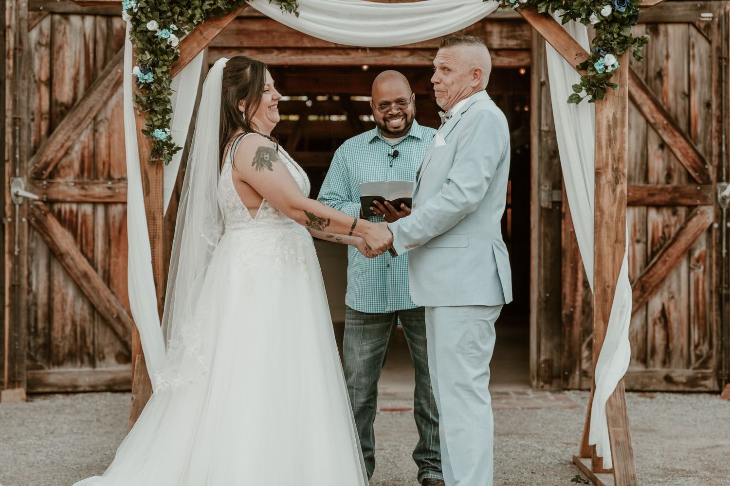A romantic couple shares tender moments at a rustic barn wedding venue decorated with greenery and white drapes.