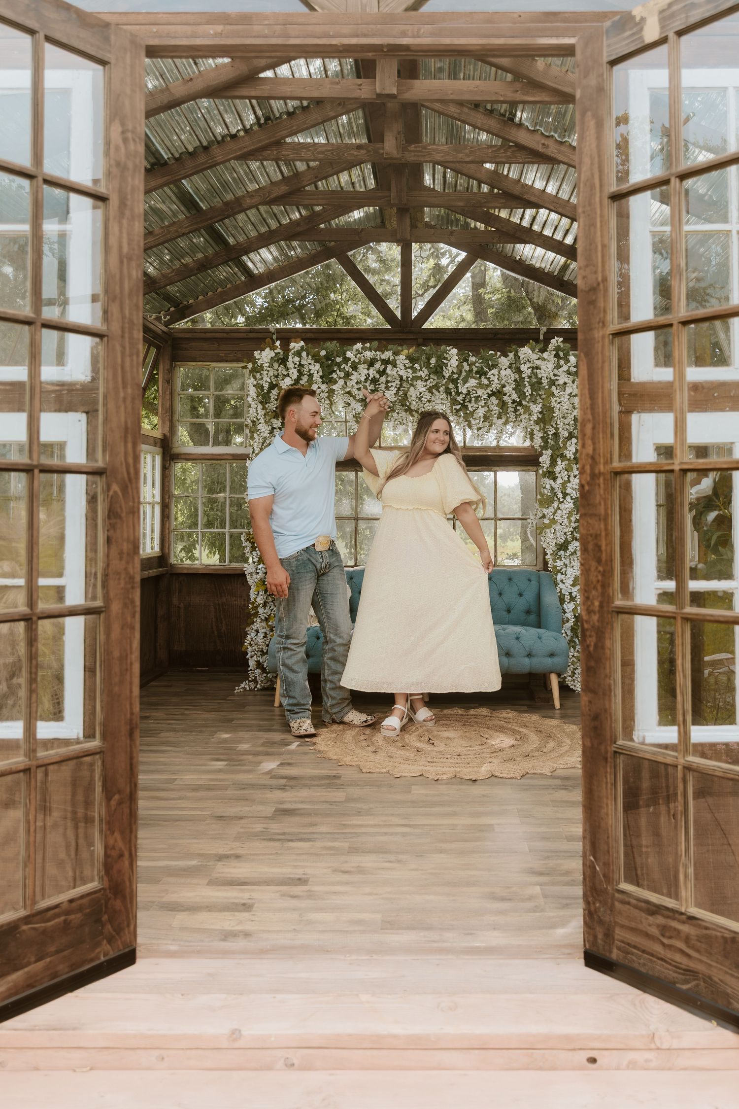 Couple dancing in a rustic greenhouse wedding venue with wood beams, floral backdrop, and French doors.
