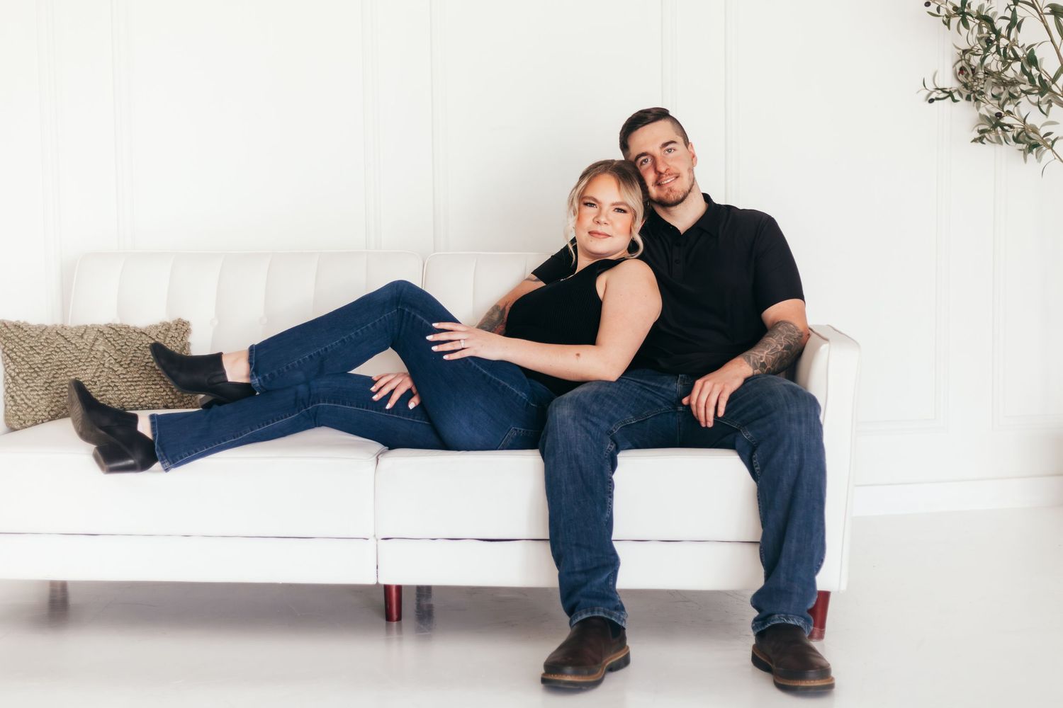 Couple relaxing together on white couch during casual photoshoot.