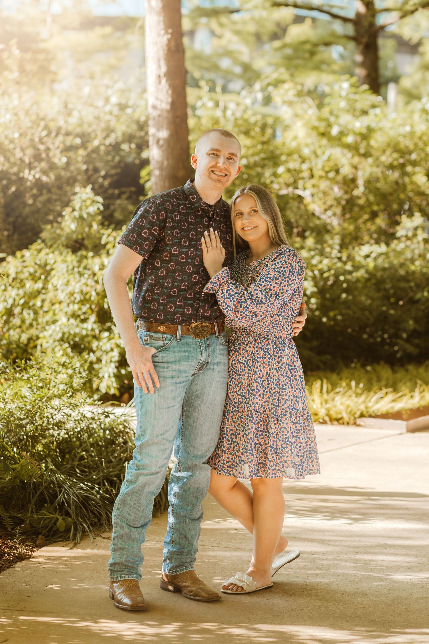 Couple posing on garden path during golden hour with sunlit foliage in background.