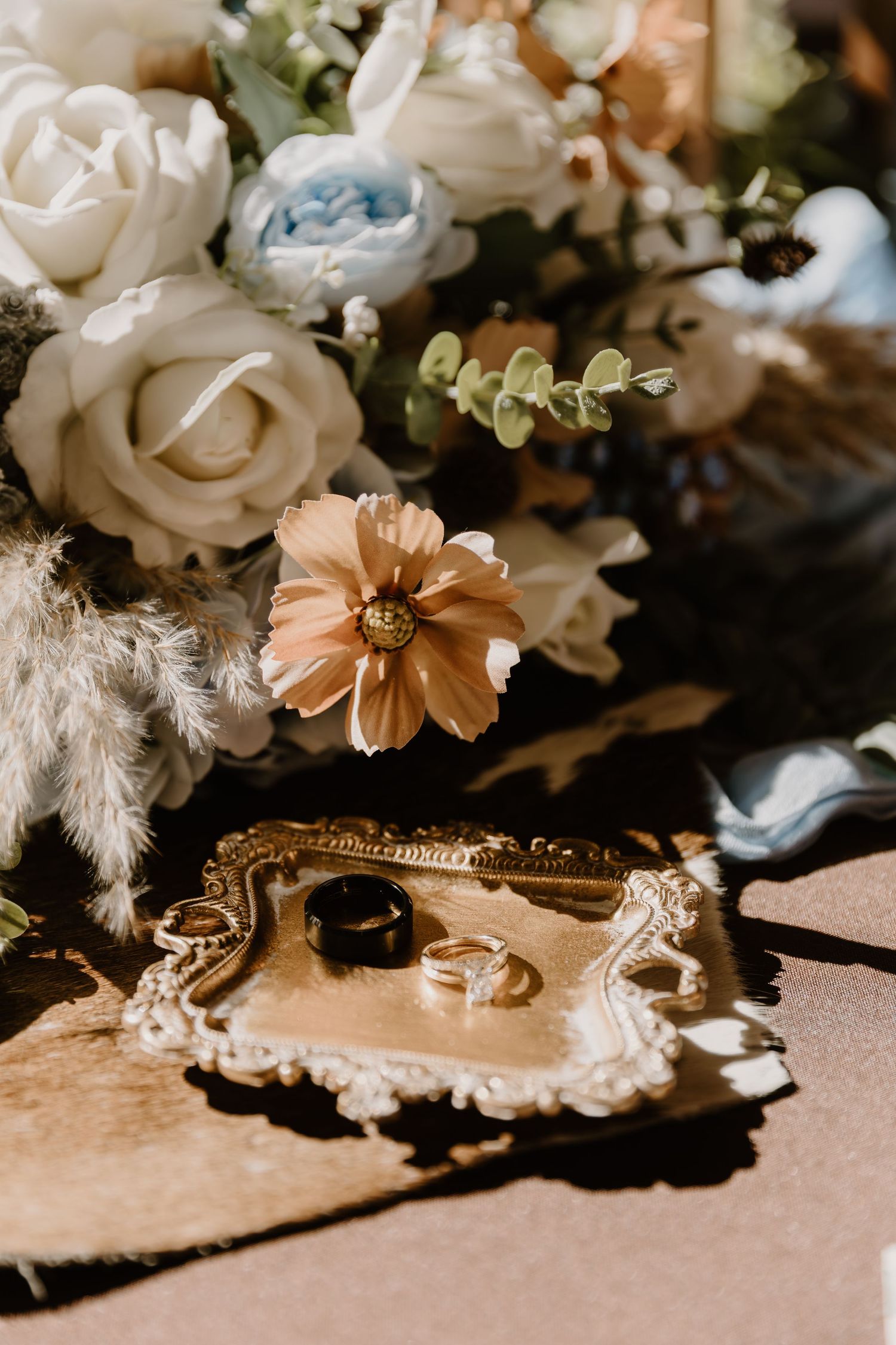 Wedding rings and delicate floral arrangements with white roses and peach blooms against a soft beige background.